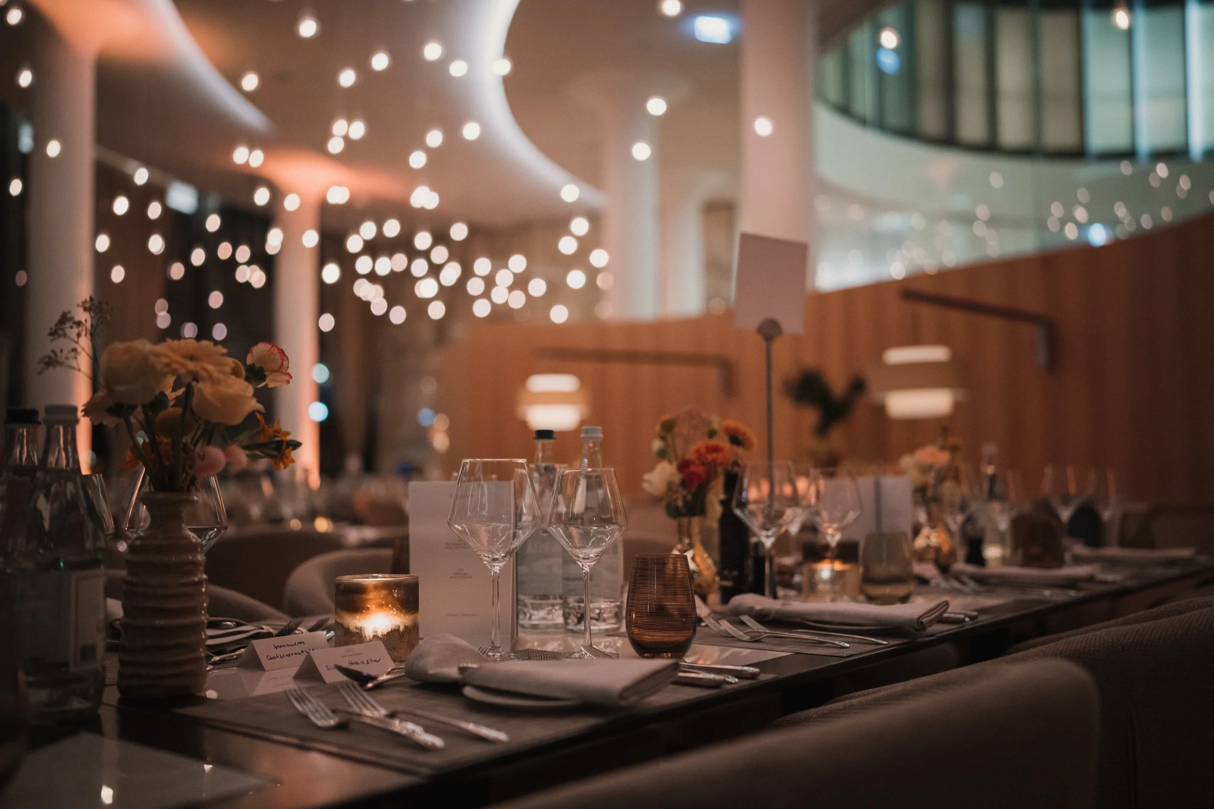 Eleganter Abendessenraum mit gedecktem Tisch, Blumen, Kerzen und Gläsern, in gemütlicher Beleuchtung, wahrscheinlich für eine Veranstaltung oder Feier.