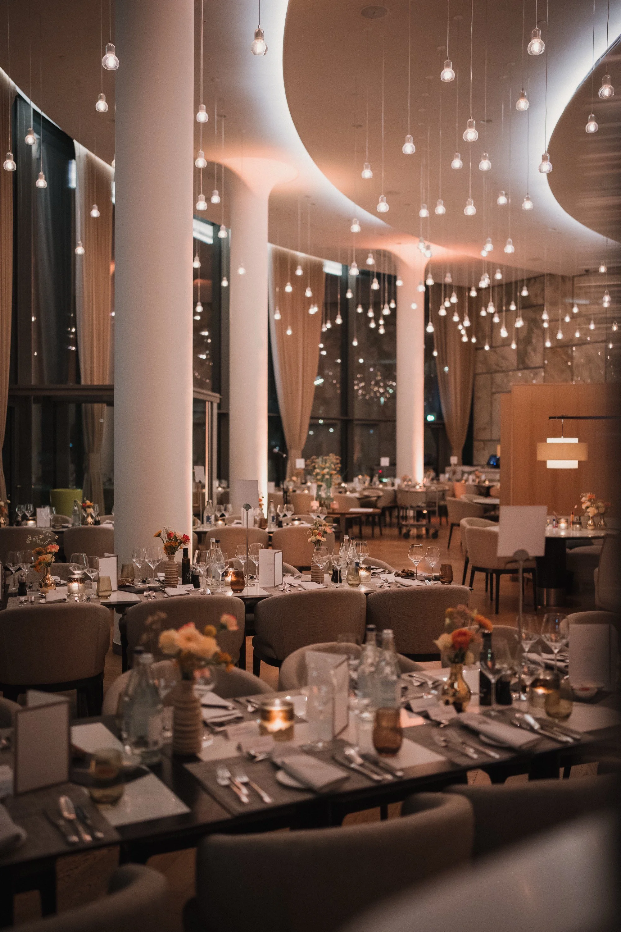 Eleganter, gut gedeckter Veranstaltungsraum mit Tischen, Stühlen, Kerzen, Blumen und Weinrosen bei Abendbeleuchtung.