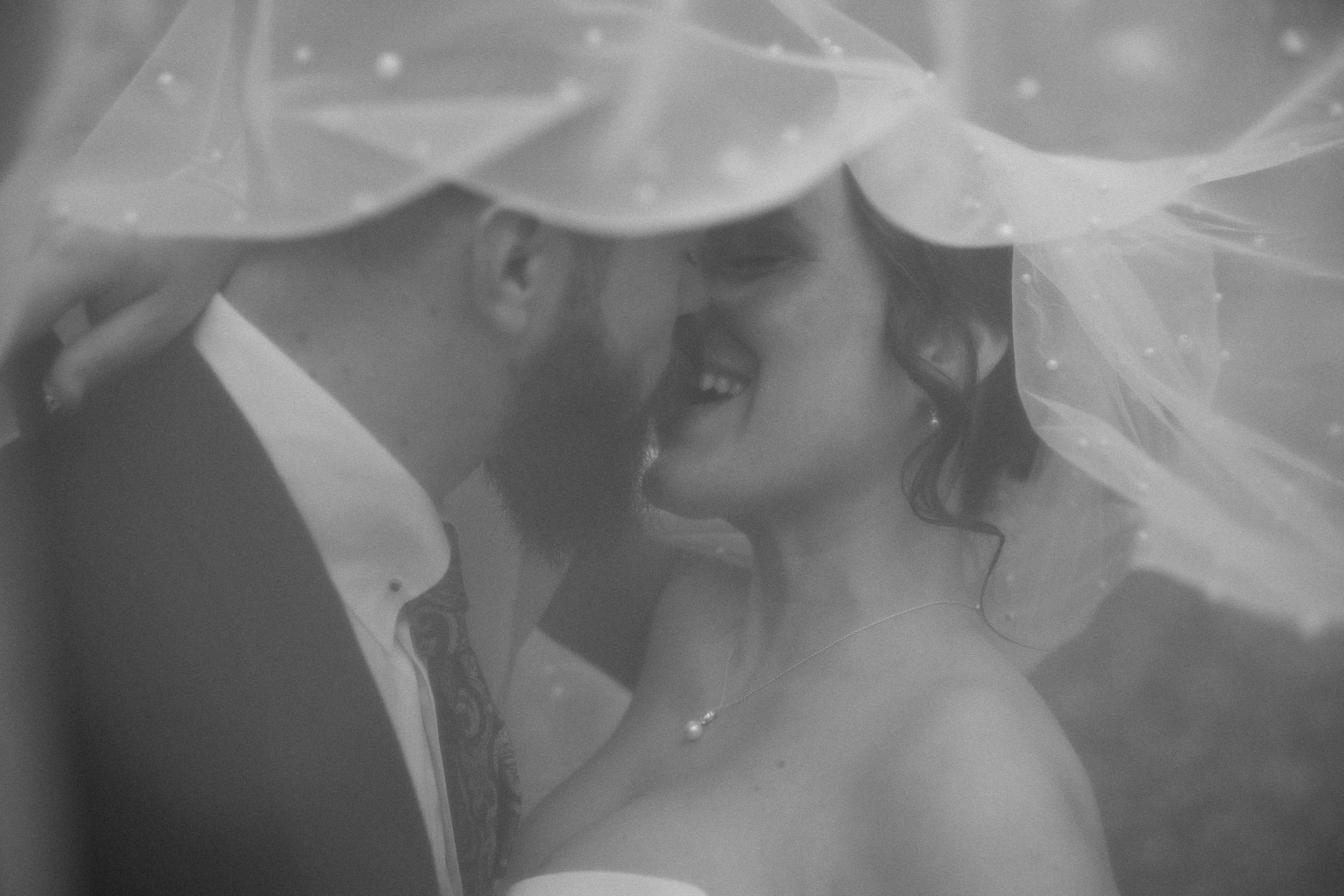 Ein Brautpaar steht dicht beieinander unter einem Schleier, sie lächelt und schaut den Bräutigam an.