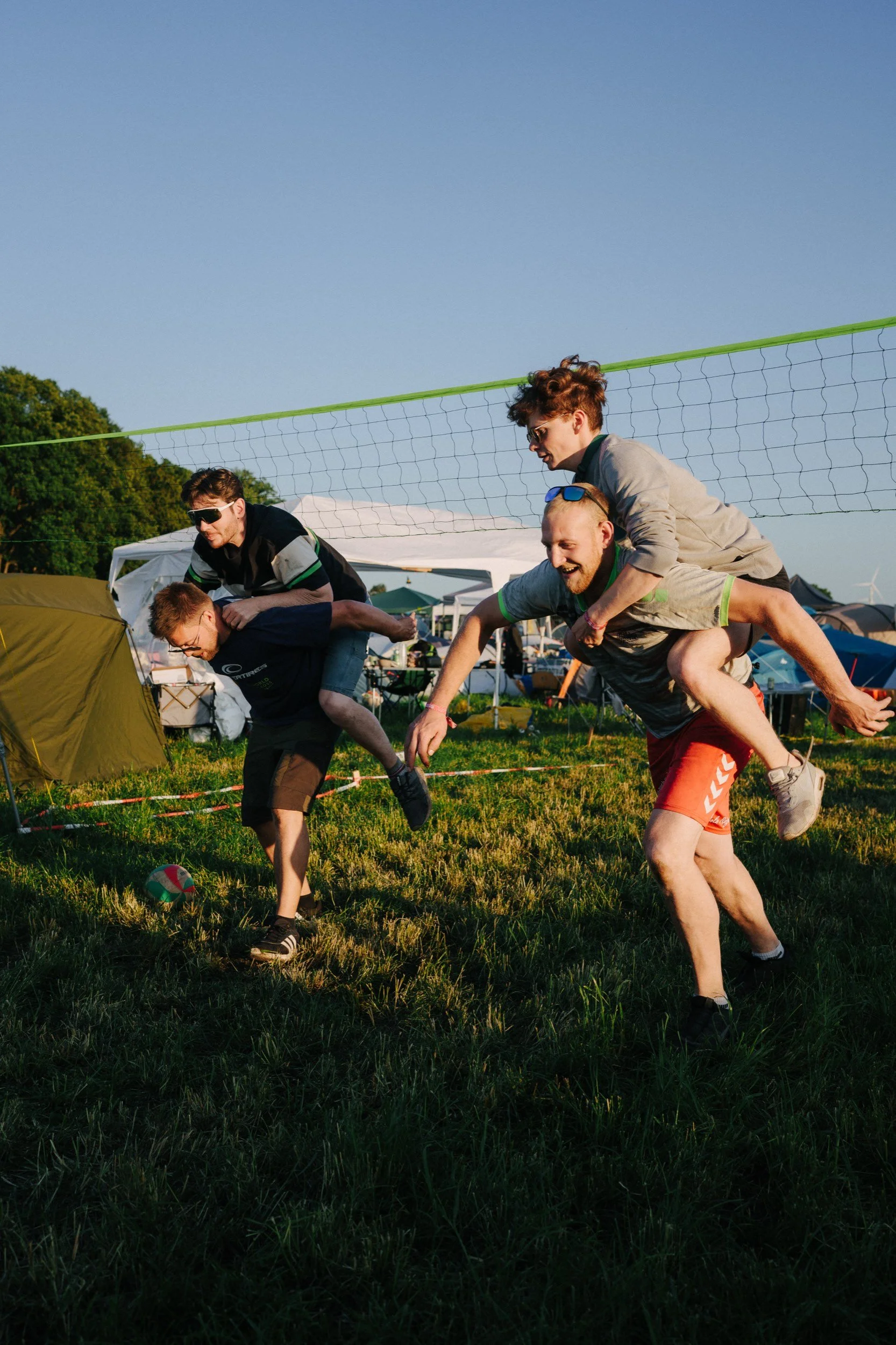 Menschen spielen Volleyball im Freien, während sie auf einem Spielfeld sitzen, mit Zelten im Hintergrund bei Sonnenuntergang.