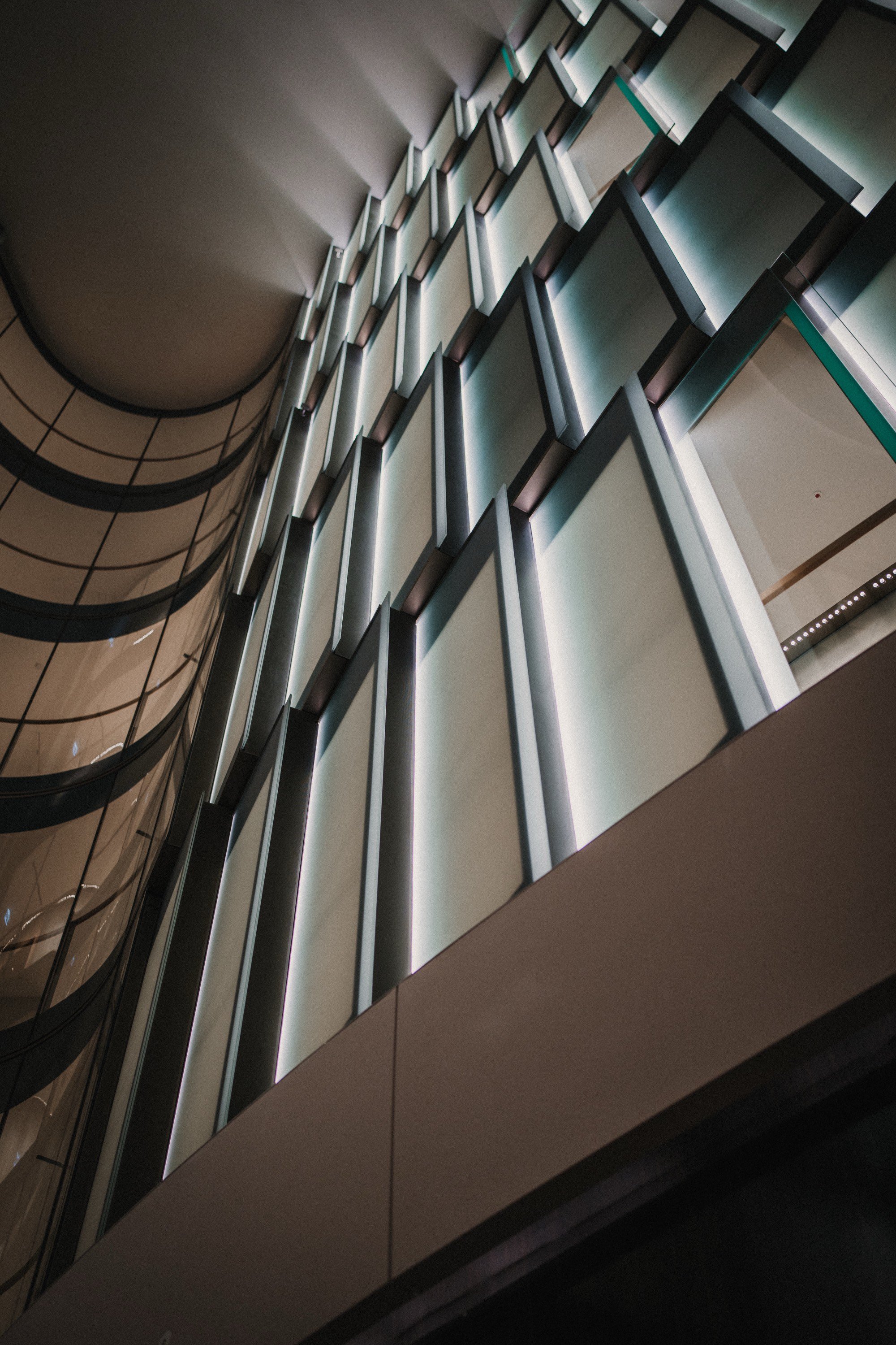 Innenansicht eines modernen Gebäudes mit beleuchteten, geometrischen Fensterdesigns, die vertikal angeordnet sind.