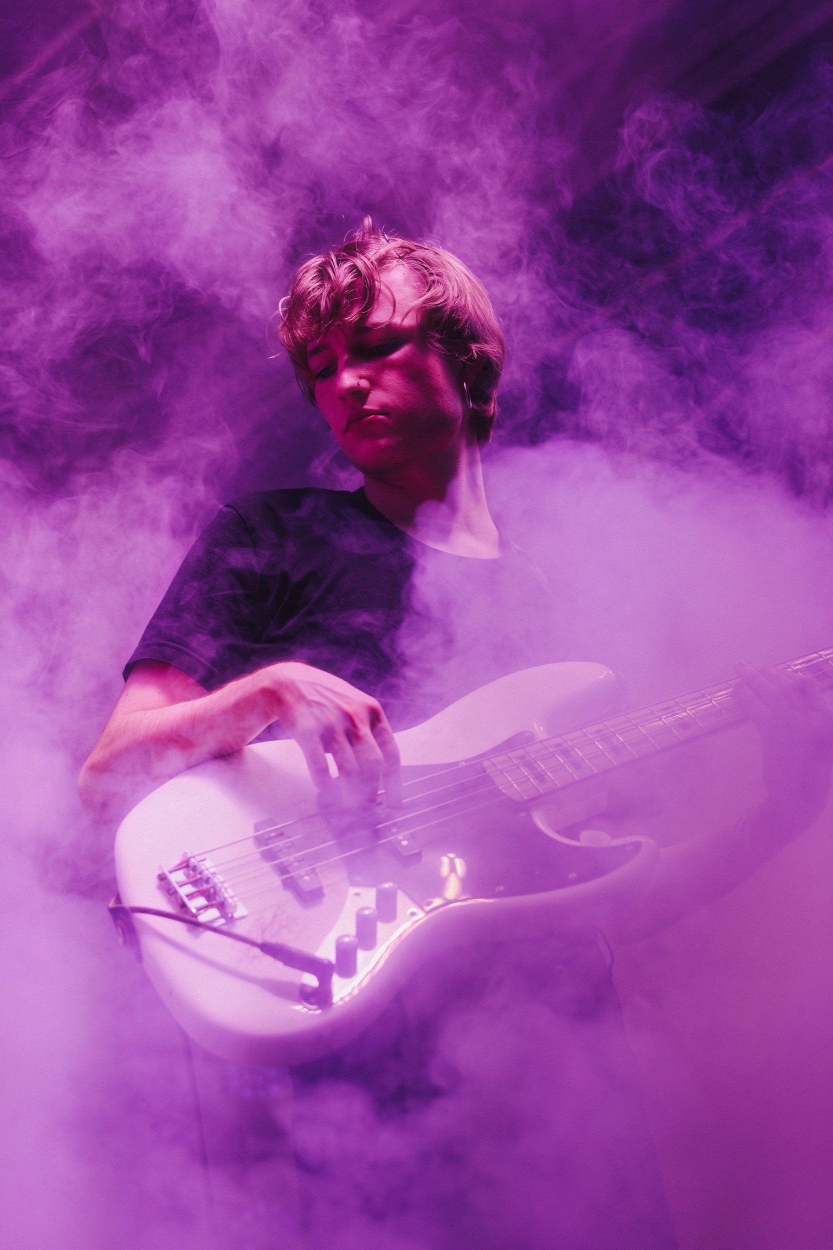 Junger Musiker spielt E-Gitarre in Rauch- und Lichteffekten, umgeben von violettem Rauch.