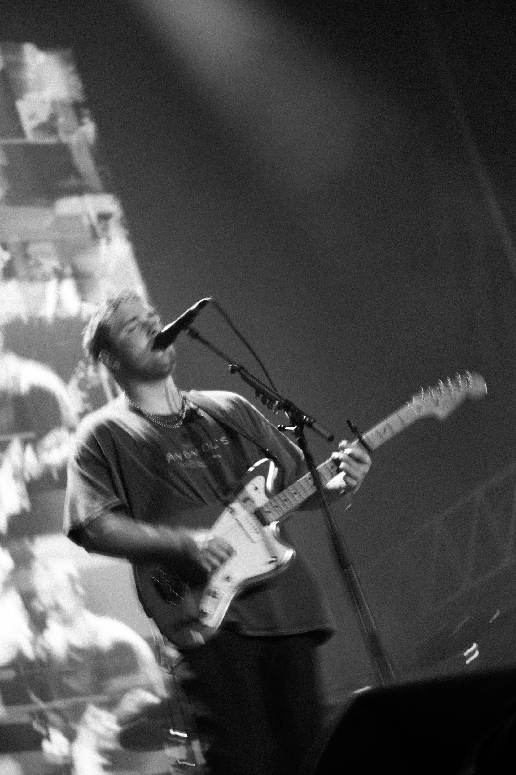 Ein Mann spielt Gitarre und singt an einem Mikrofon auf einer Bühne, schwarz-weiß