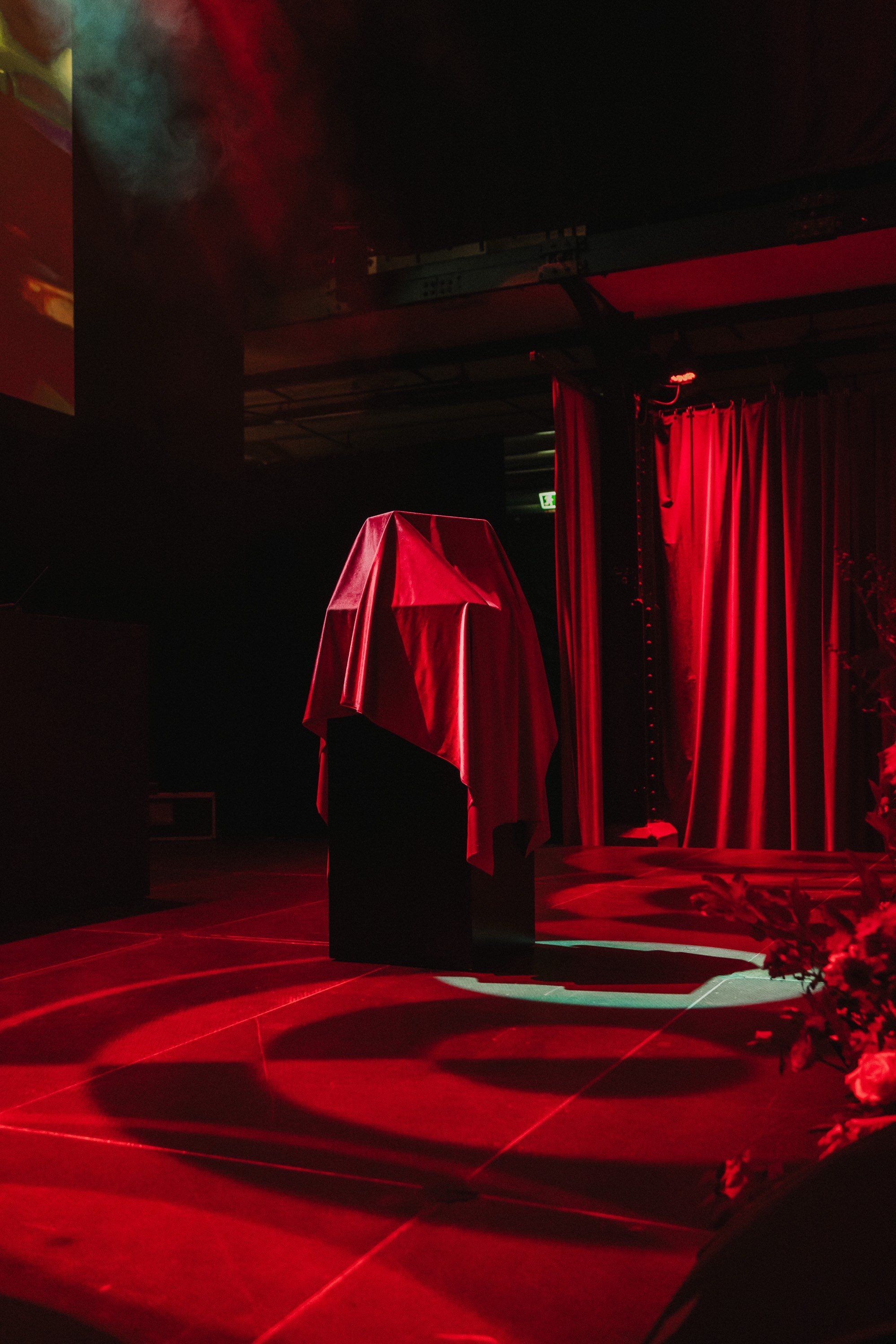 Bühne mit einer Statue, die mit einem roten Tuch bedeckt ist, im Theater oder Veranstaltungsraum, Beleuchtung in rotem Licht, rote Vorhänge im Hintergrund.