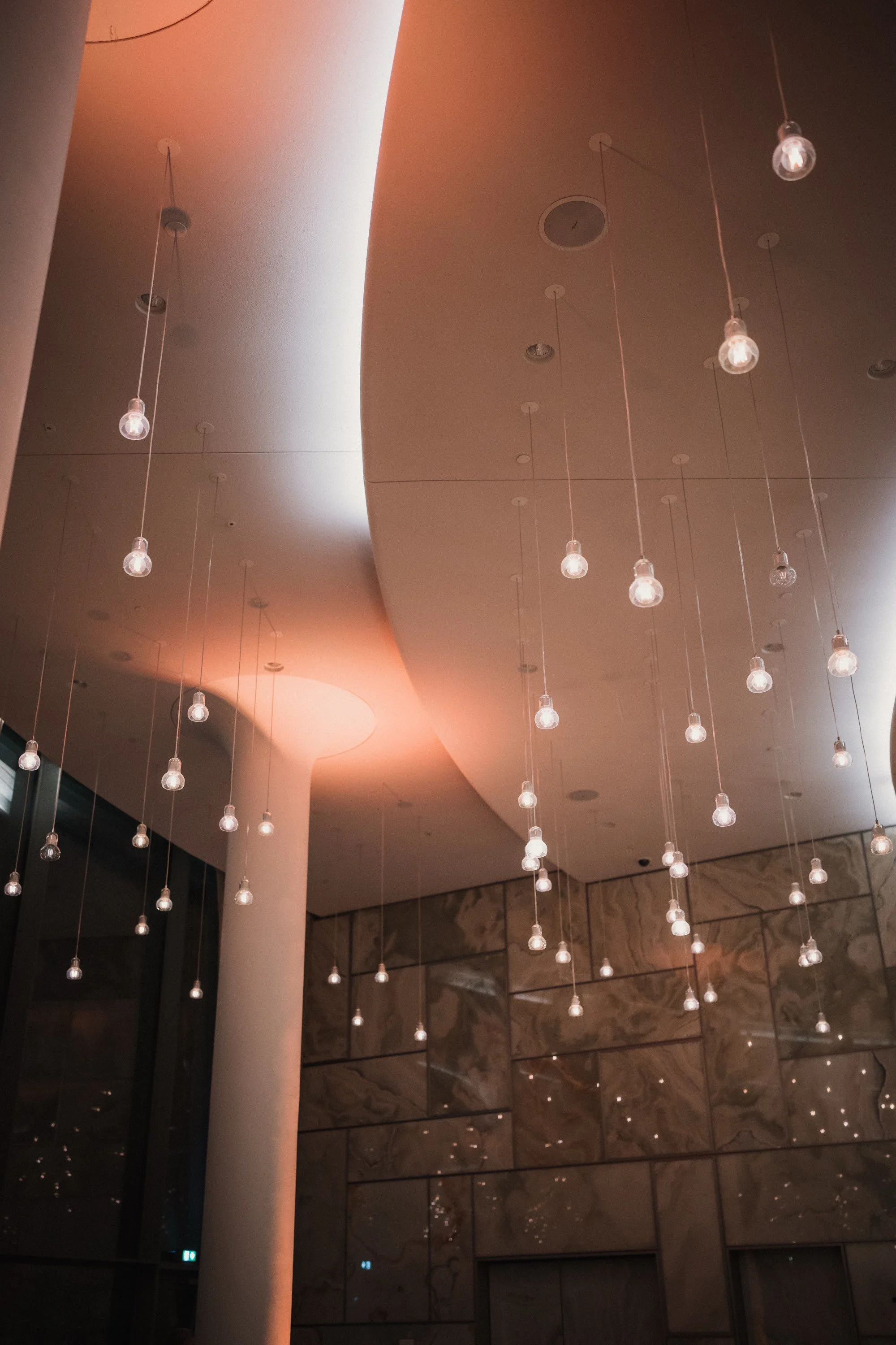 Moderne Innenarchitektur mit vielen kleinen hängenden Lichtbulbs und geschwungenem Deckenbereich in warmem Licht.