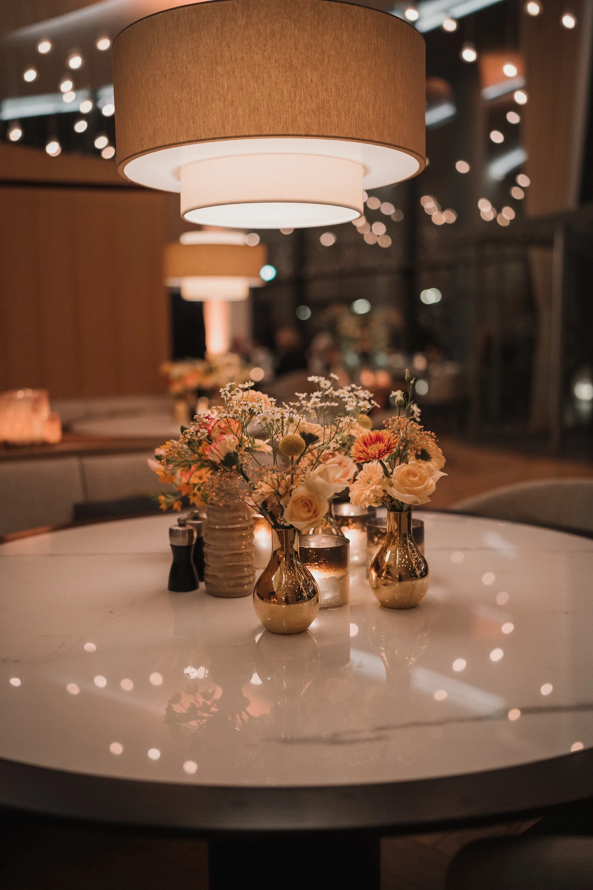 Tisch mit Blumen, Kerzen und Lampenschirm in einem Restaurant bei Abendlicht.