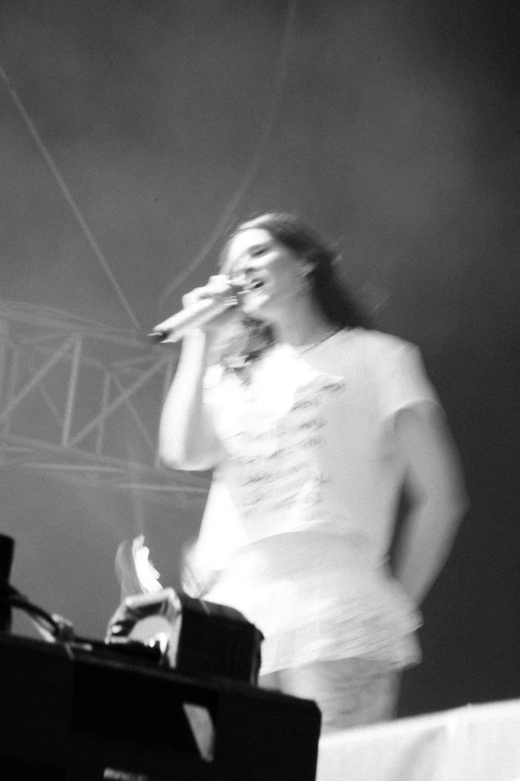 Eine lächelnde junge Frau singt mit einem Mikrofon auf einer Bühne, im schwarzen und weißen Bild.