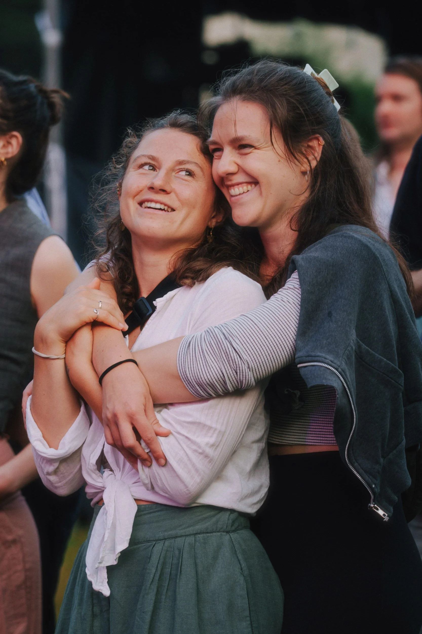 Zwei lachende Frauen umarmen sich bei einer Feier im Freien.