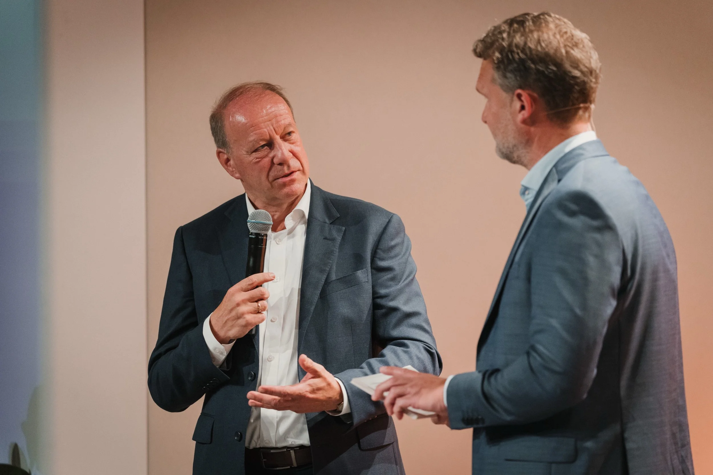 Zwei Männer in Anzügen führen ein Gespräch bei einer Veranstaltung.