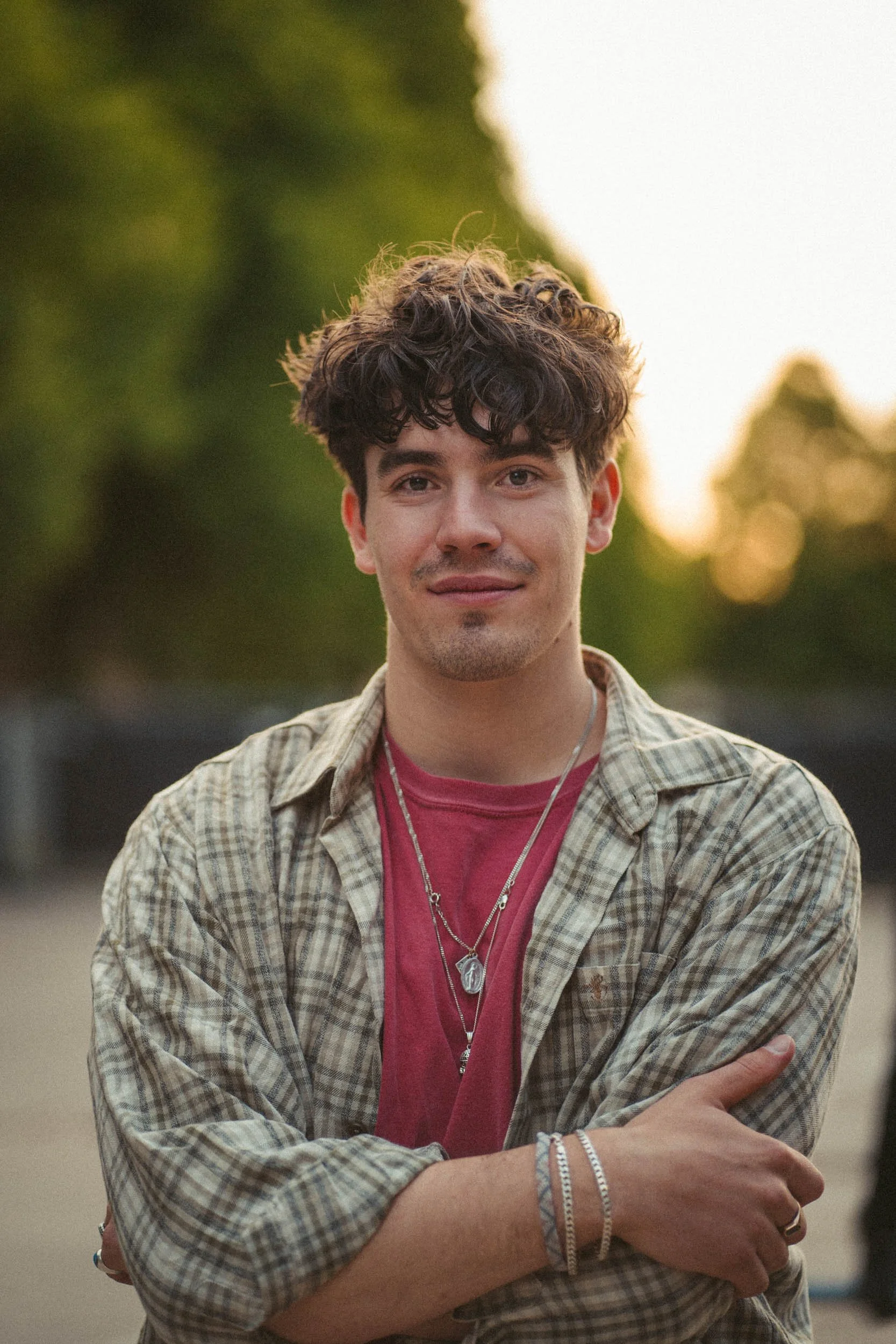 Der Musiker Edwin Rosen steht im Freien mit verschränkten Armen, trägt mehrere Ketten und Armbänder, hat dunkel gekräuseltes Haar und trägt ein rot-beiges kariertes Hemd.