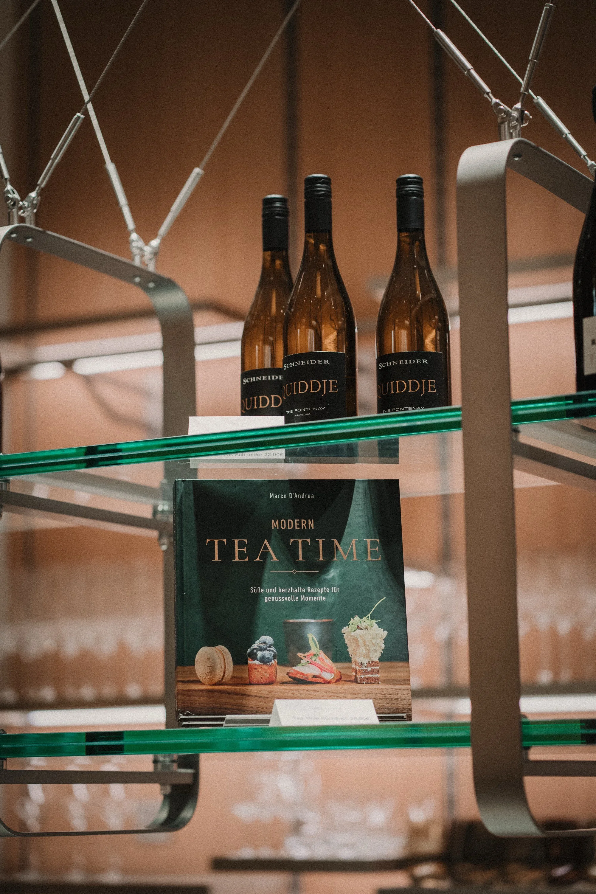 Drei Flaschen Wein stehen auf einem Regal, darunter befindet sich ein Buch mit dem Titel "Modern Tea Time" und einem Bild von Desserts auf dem Cover.