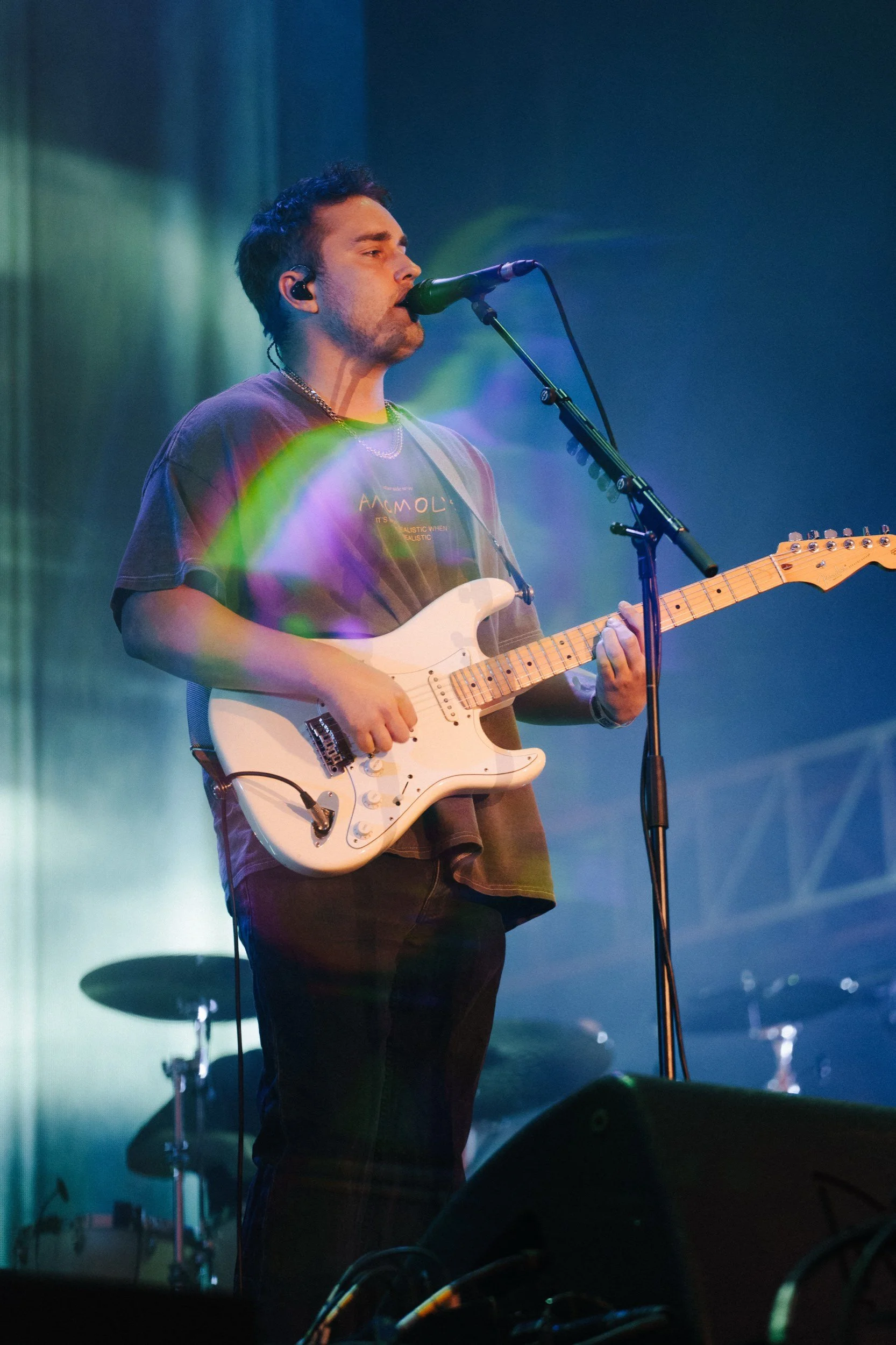 Ein junger Mann spielt Gitarre und singt in einem dunklen Raum, mit leuchtenden Lichtern im Hintergrund.