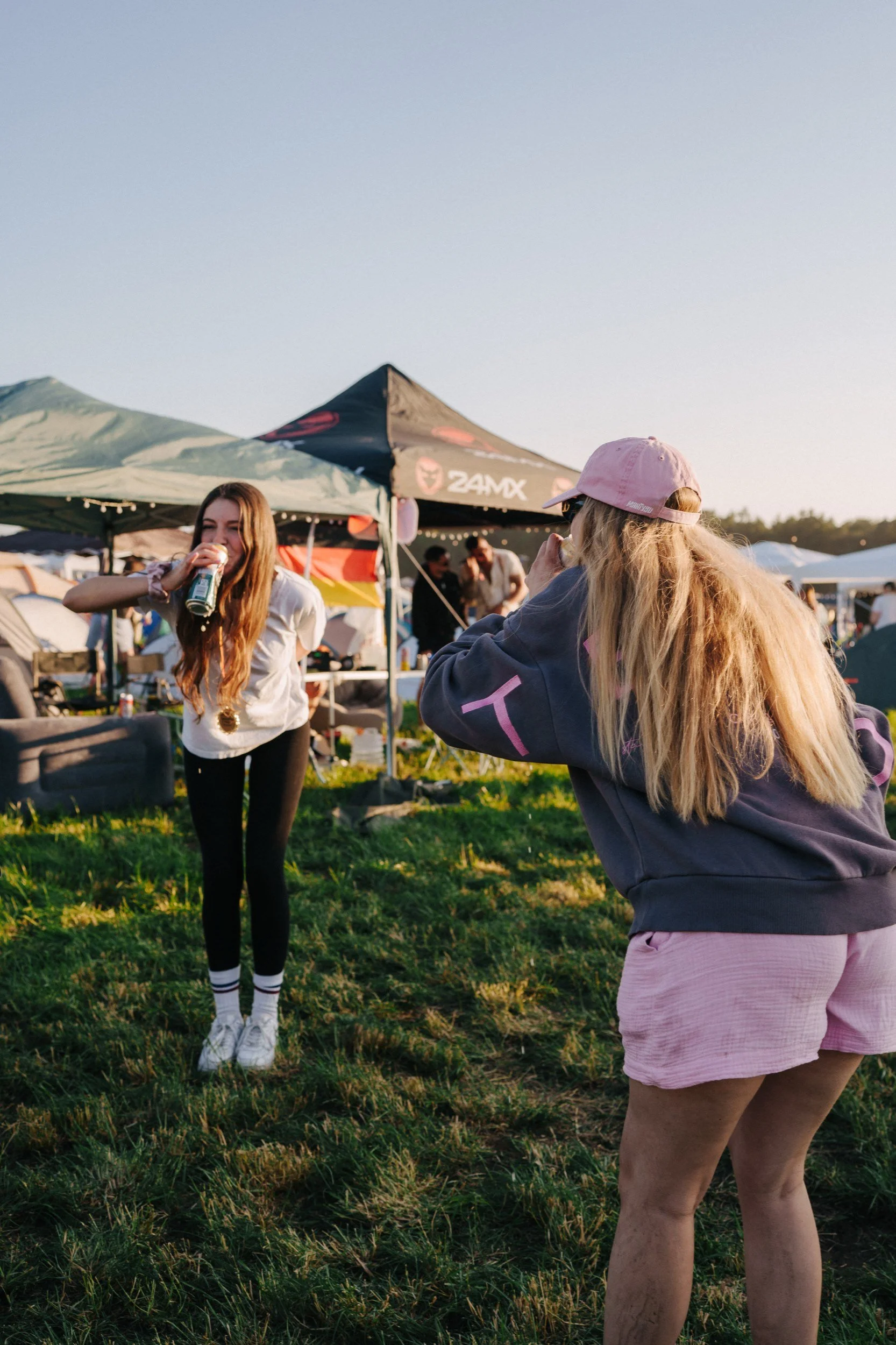 Zwei Frauen bei einem Festival im Freien, eine trinkt ein Getränk, die andere macht ein Foto.