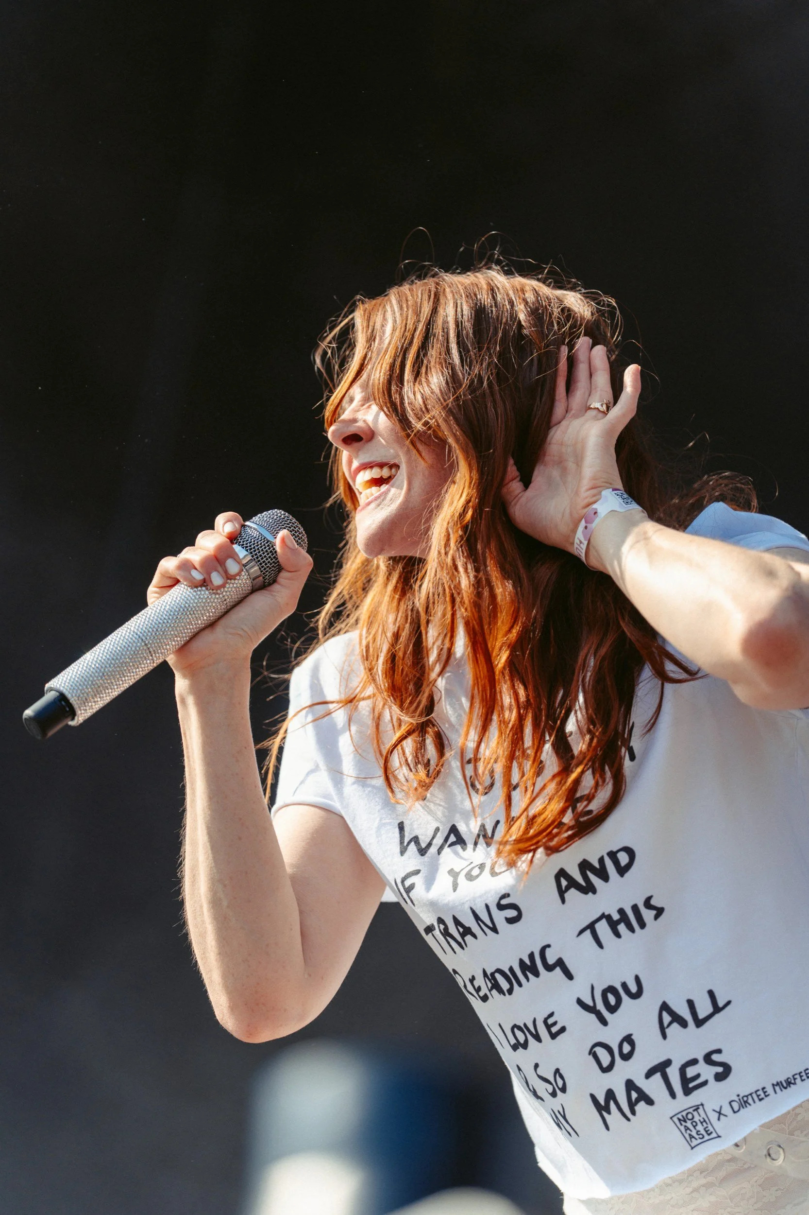Eine lachende Frau beim Singen bei einem Konzert mit einem Mikrofon in der Hand.