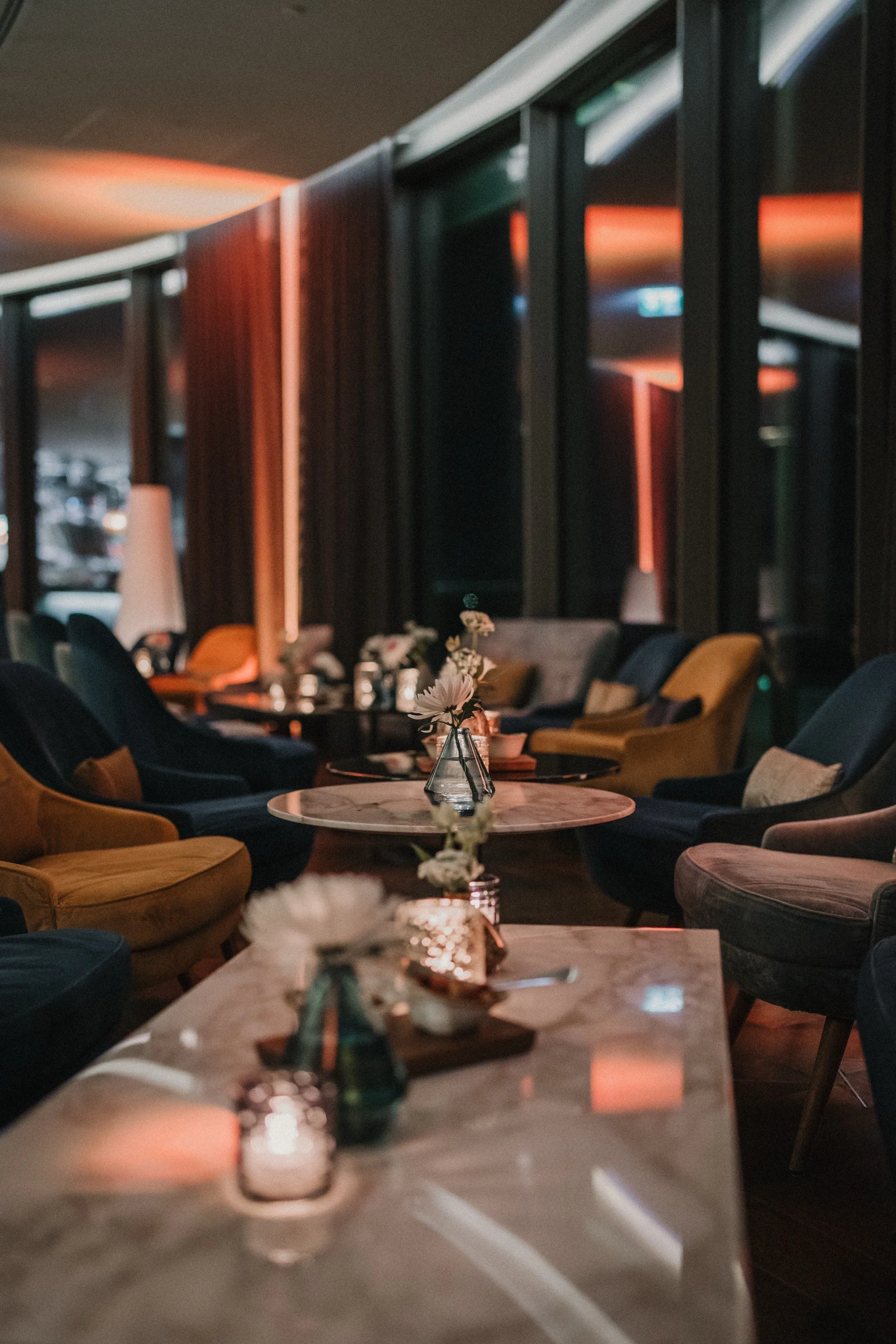 Eleganter Lounge-Bereich mit bunten Sesseln, kleinen Tischen mit Blumenvasen, Kerzen und Dekorationen, zur Abendzeit mit warmem Licht.