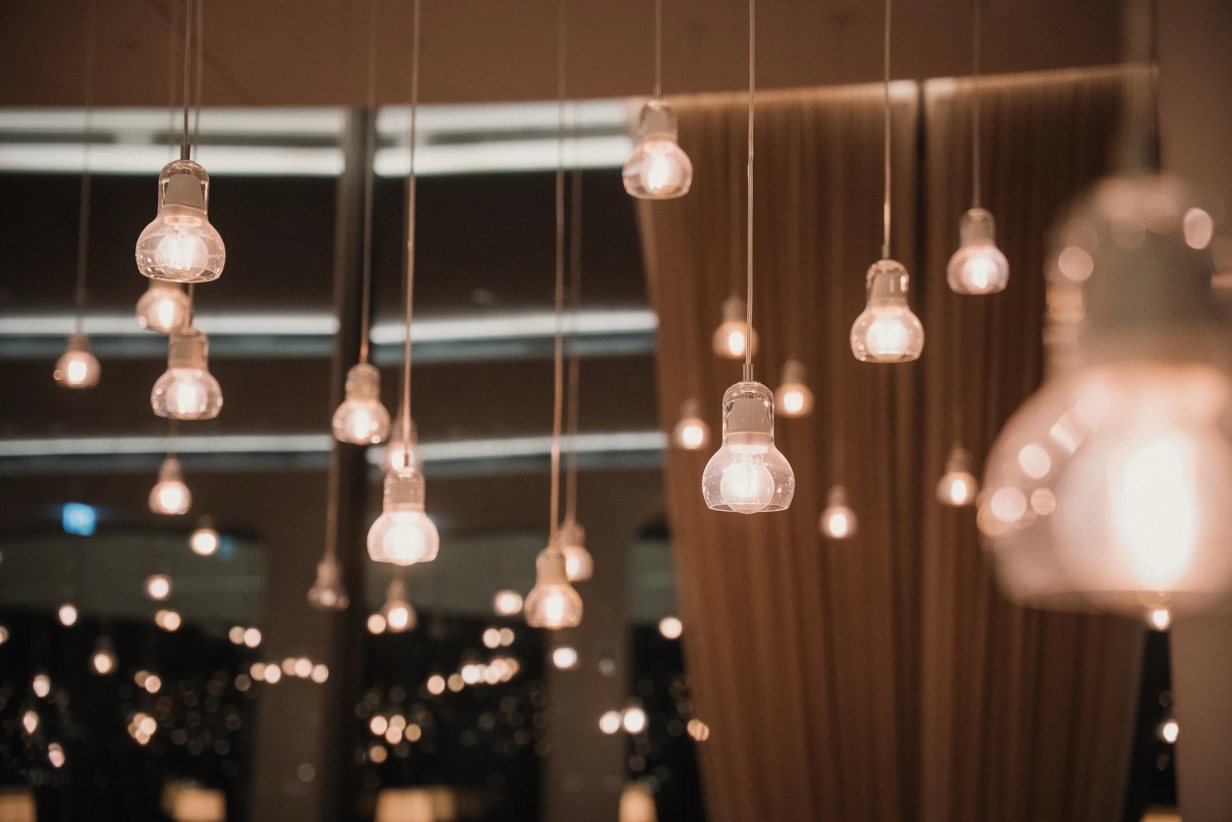 Hängende Glühbirnen in einem modern eingerichteten Raum mit dunklen Vorhängen.