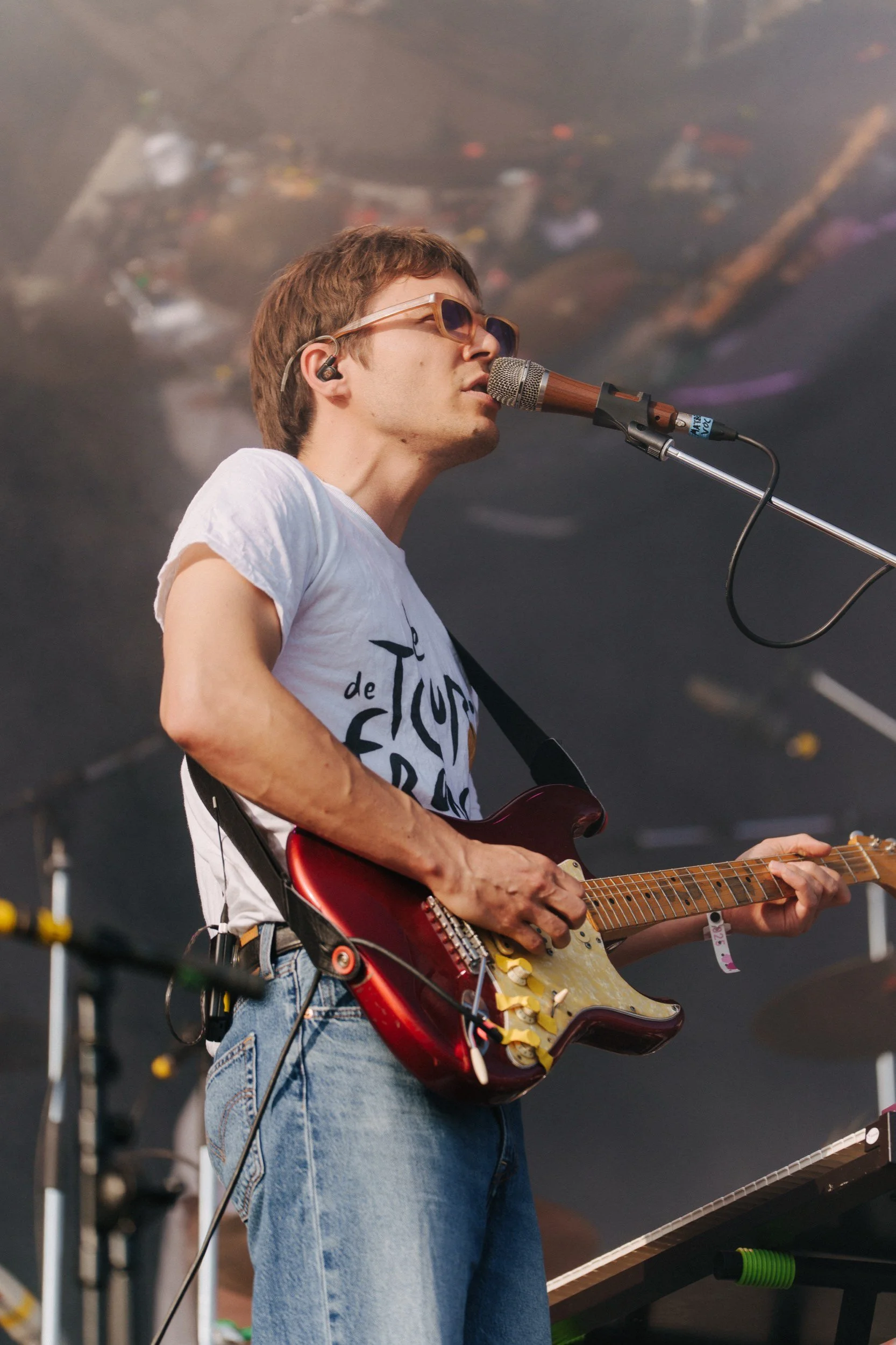Jazzmusiker spielt E-Gitarre und singt in einem Konzert, trägt weiße T-Shirt und Brille, im Hintergrund eine dunkle Kulisse.