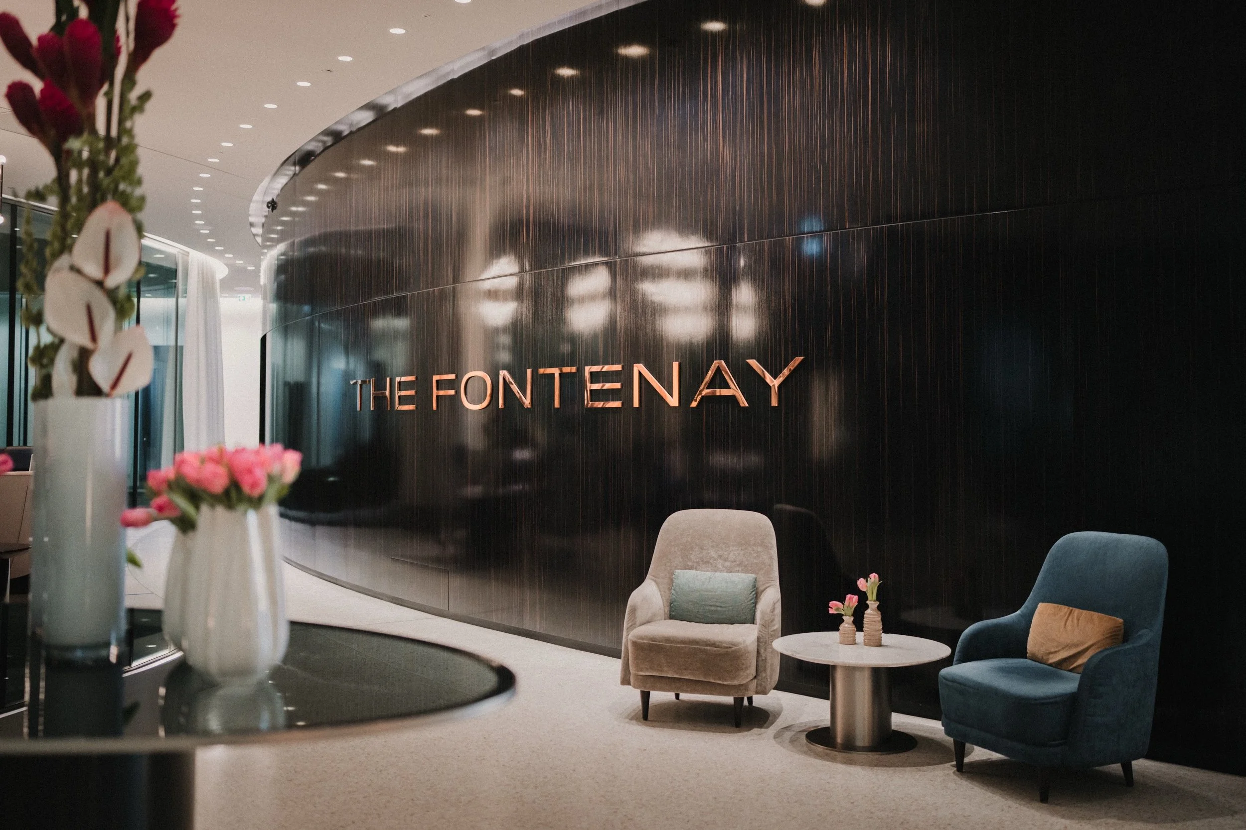 Innenansicht des Hotels The Fontenay mit modernen Sitzgelegenheiten, Vasen mit Blumen und einer schwarzen Wand mit goldener Schrift