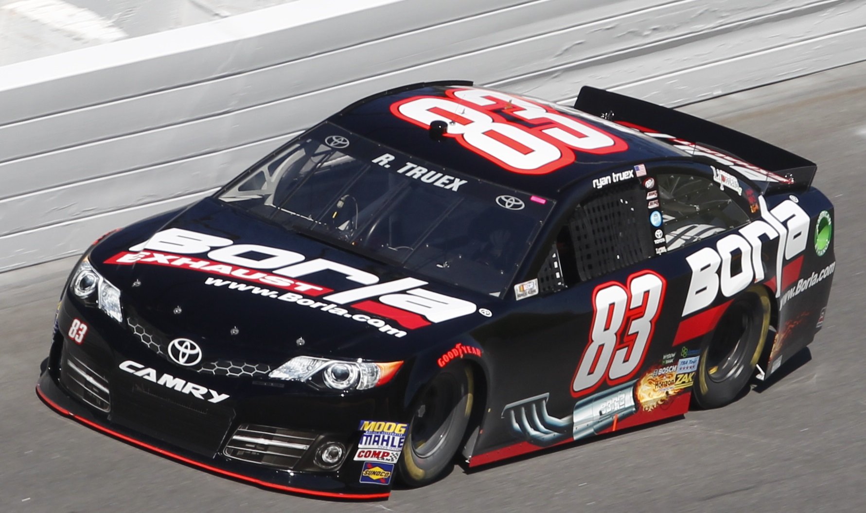 A black Toyota Camry race car with red and white branding, number 83, driving on a race track.