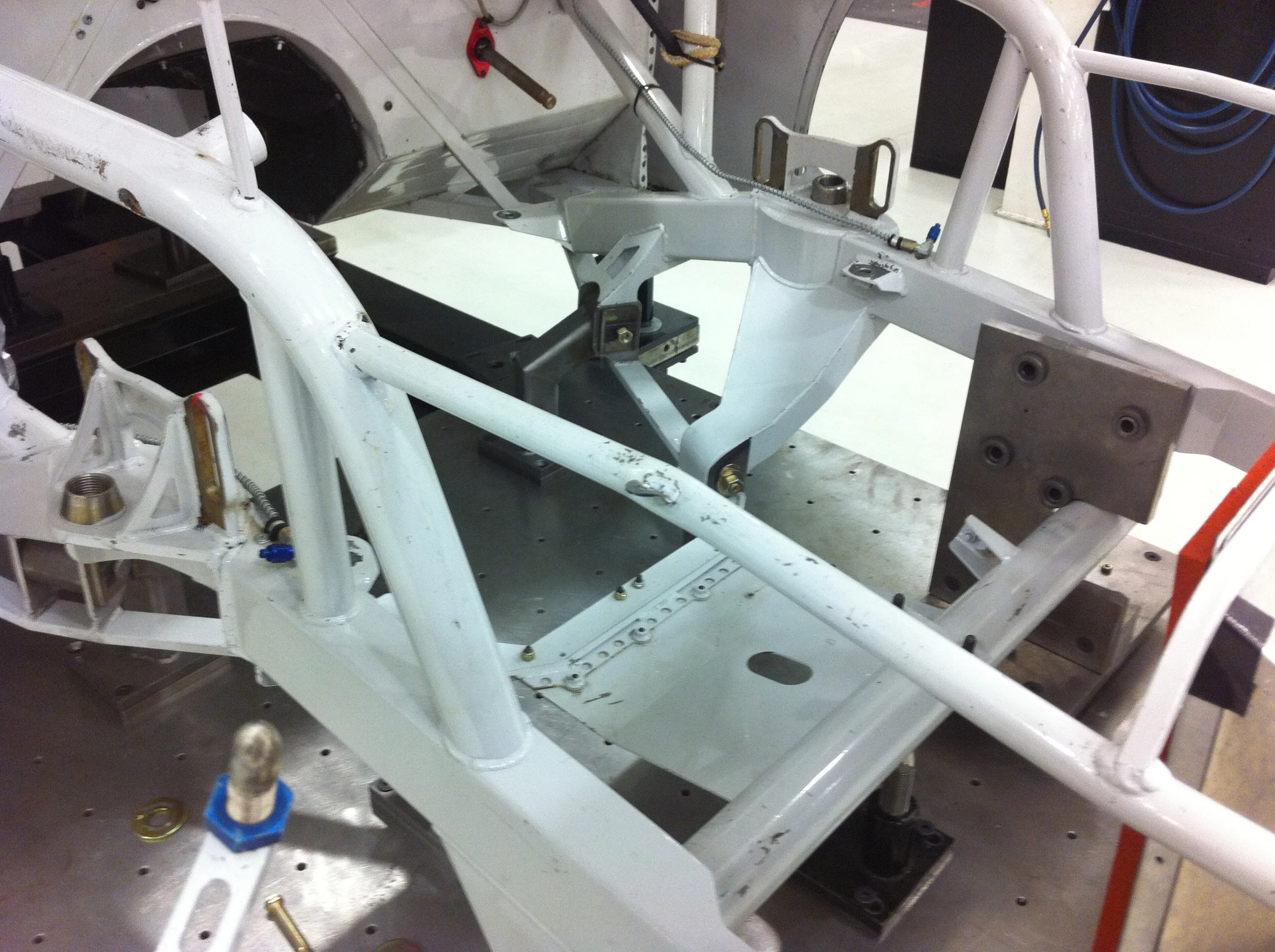 An unfinished frame of a race car with white painted metal parts and various mechanical components and tools around it.