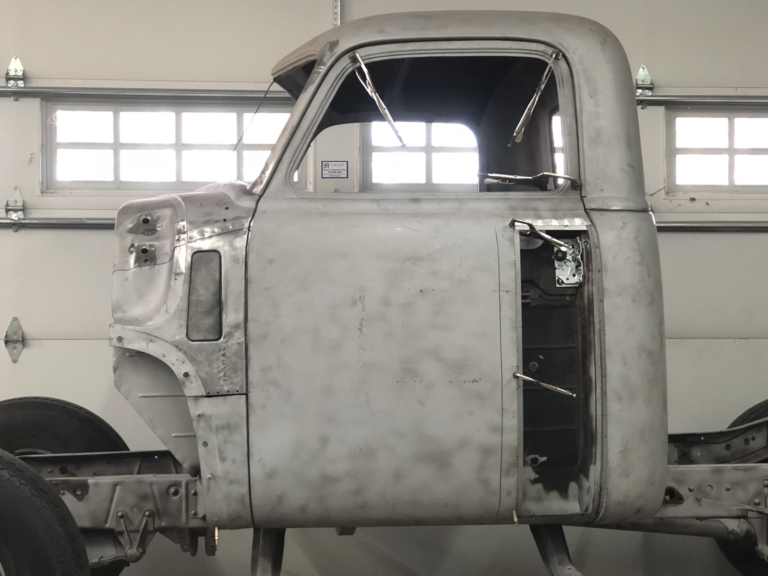 An unfinished, vintage truck cab with a metal body, parked inside a garage.