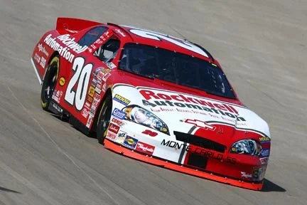 Red and white Chevrolet race car on a track with the number 20 and sponsorship logos.