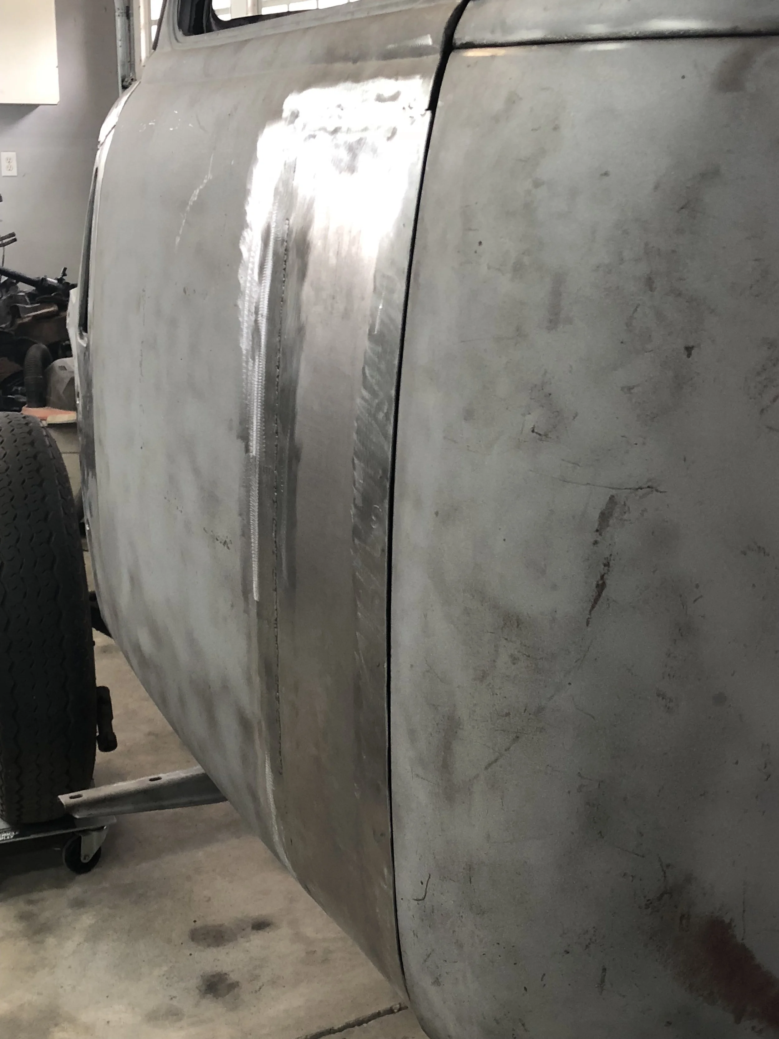 Close-up of a metal car body in a garage or workshop, showing scratches and scratches on the surface.
