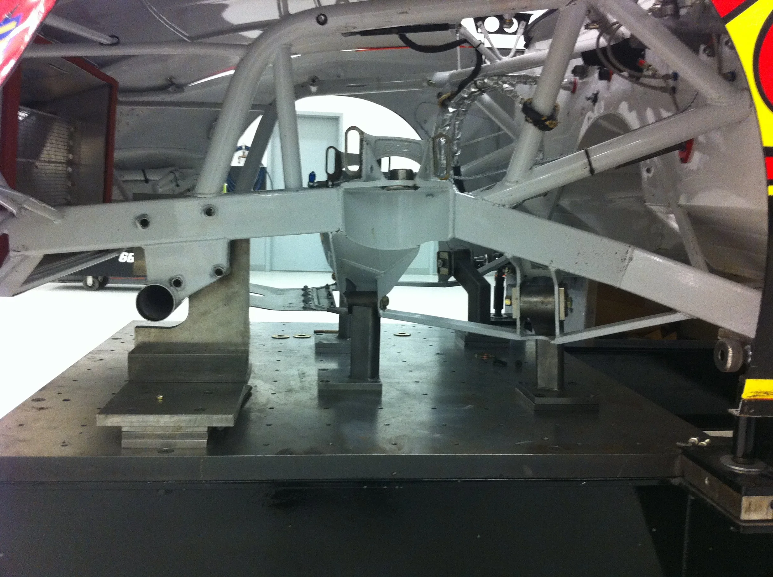 Interior view of a racing car or aircraft chassis with metal framework, mounted on a testing platform in a laboratory or workshop setting.