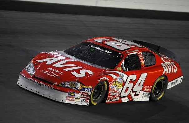 Red and white race car with the number 64, driving on a race track.