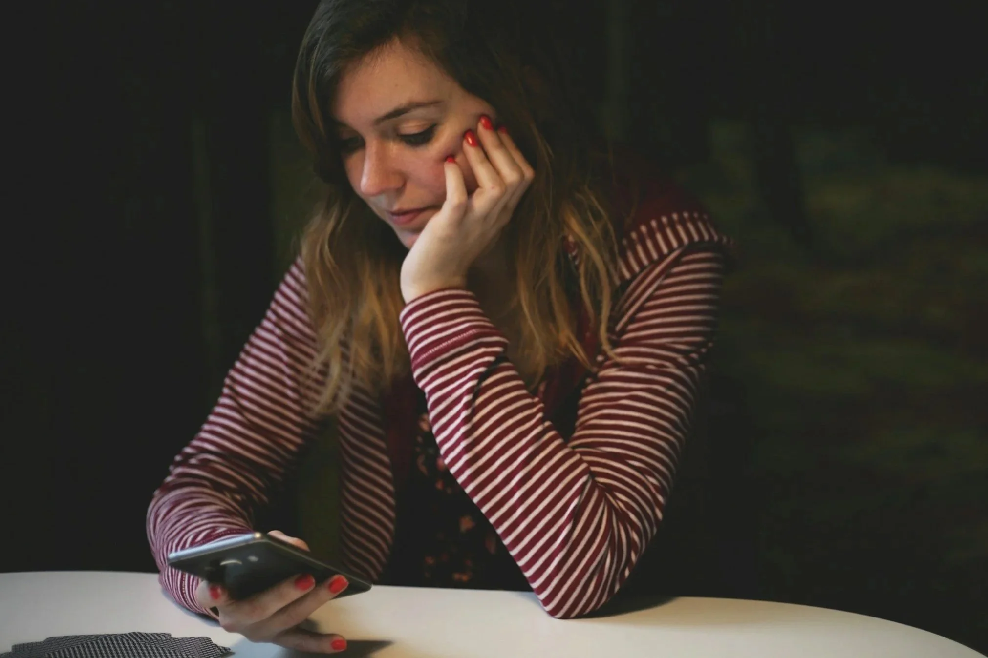 Mulher sentada à mesa com celular na mão