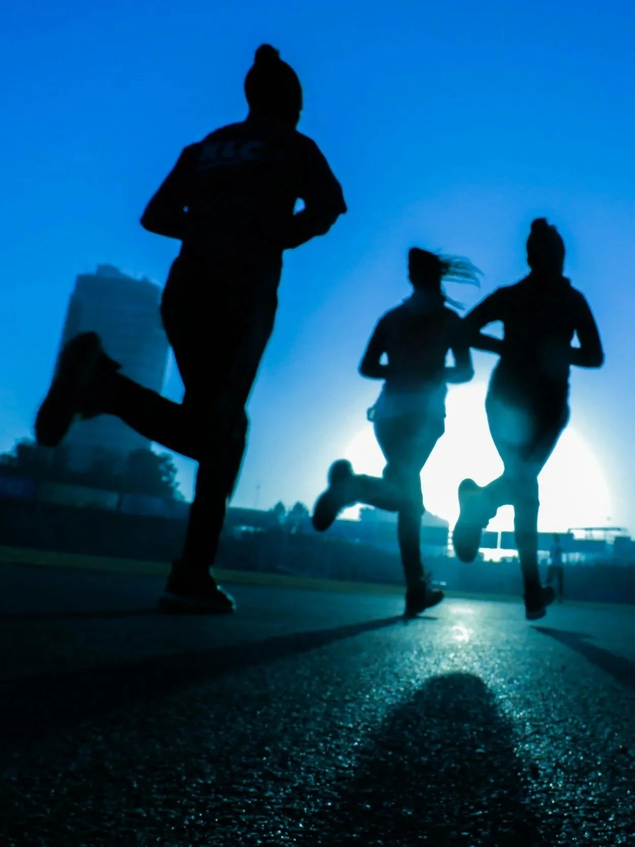 Silhouettes of three people running outdoors at sunrise or sunset.
