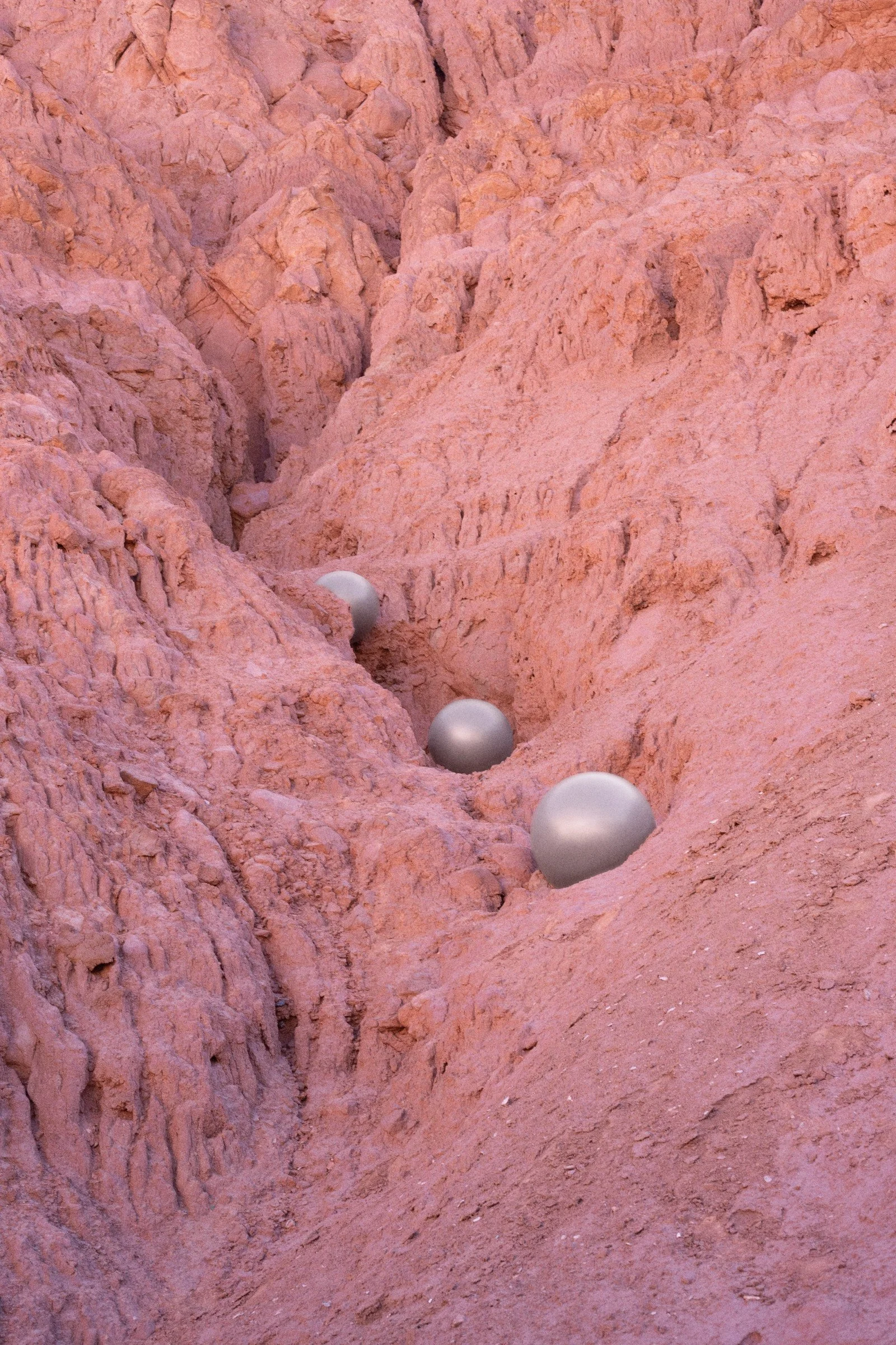 A rocky, pink-colored landscape with a series of six silver metallic balls arranged diagonally across a narrow, creviced terrain.