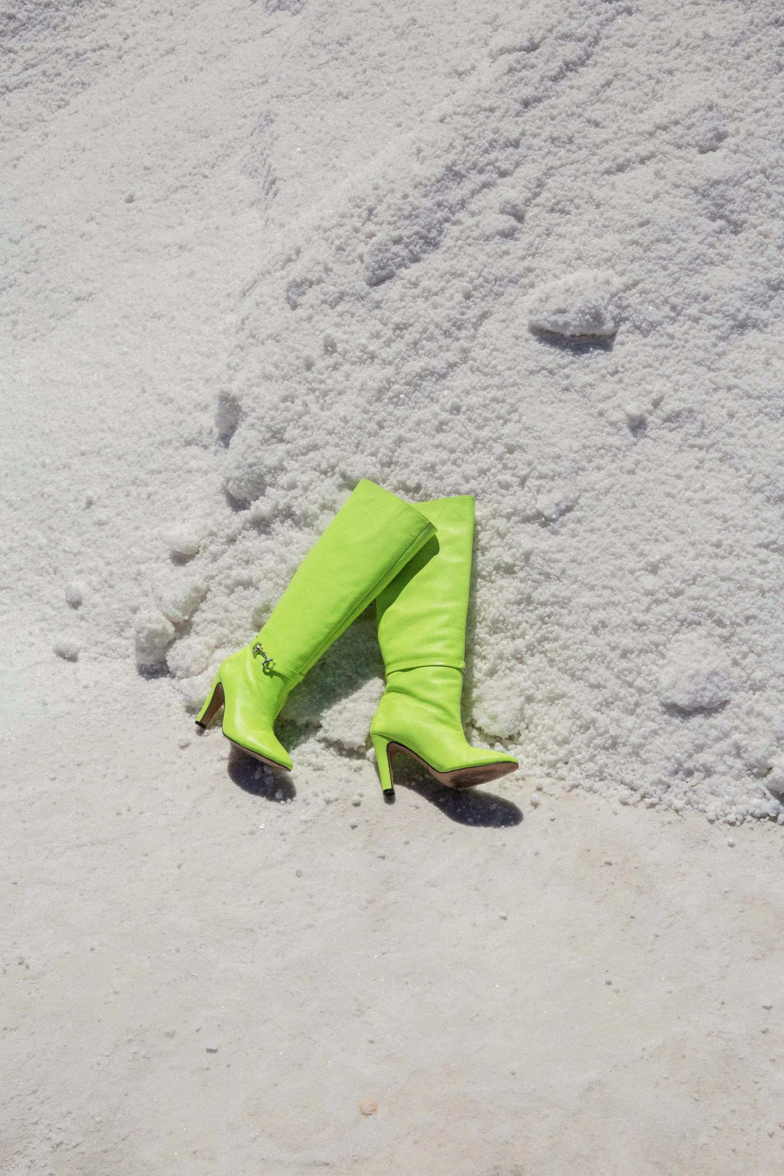 Bright yellow high-heeled boots lying on snow with footprints nearby.