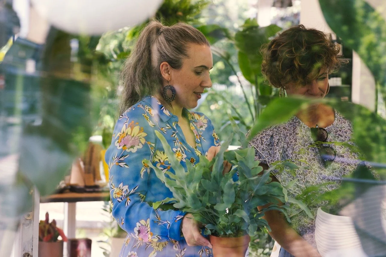 Zwei Frauen wählen gemeinsam eine Zimmerpflanze im lichtdurchfluteten Prana Station Store in Hamburg, natürliche Atmosphäre mit viel Grün.