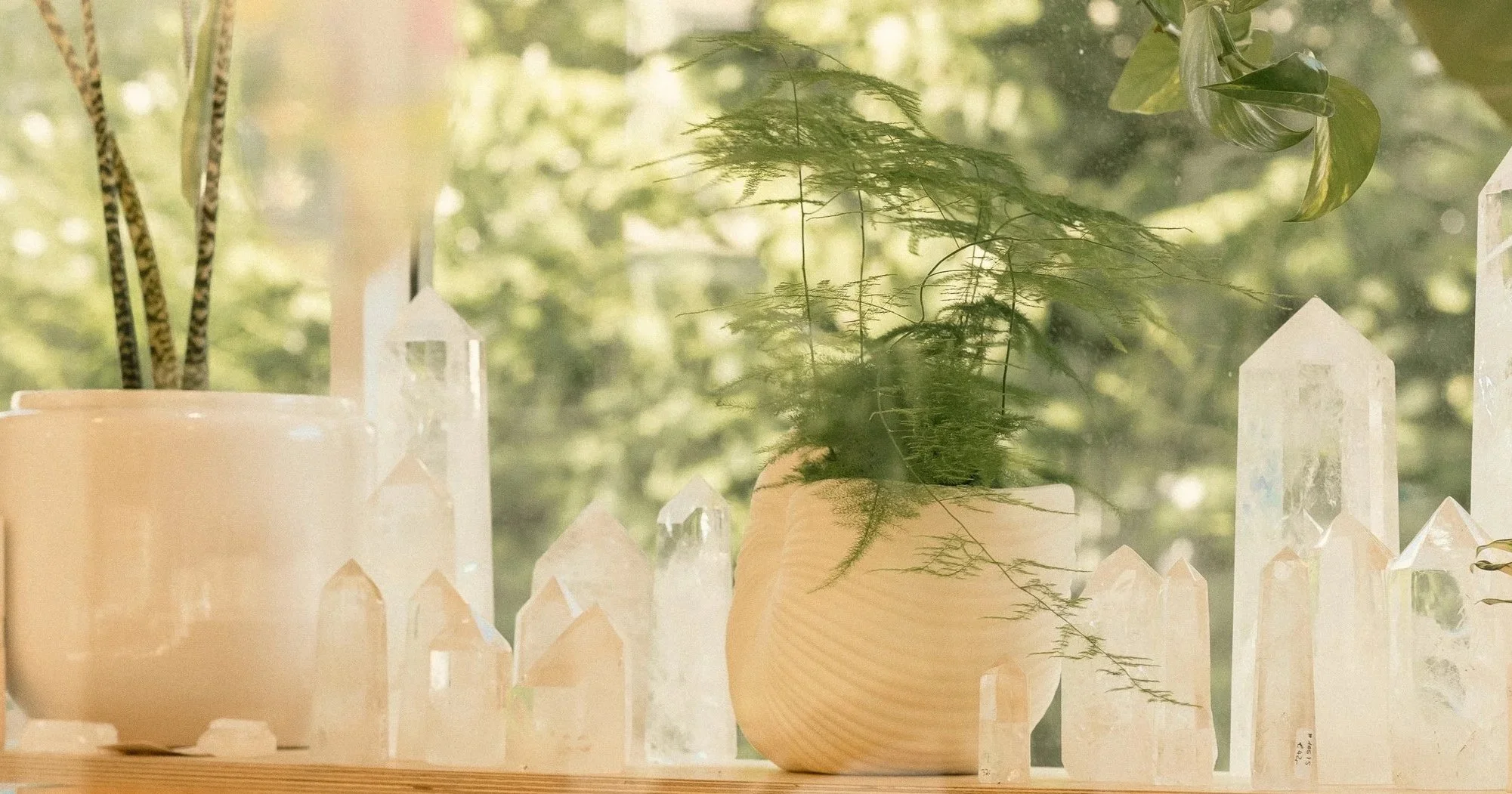 Stimmungsvolles Stillleben mit weißen Kerzen und klaren Bergkristallen in natürlicher Umgebung, sanftes Tageslicht, grüne Pflanzen im Hintergrund, ruhige und harmonische Atmosphäre für Achtsamkeit, Spiritualität und Wohlbefinden.