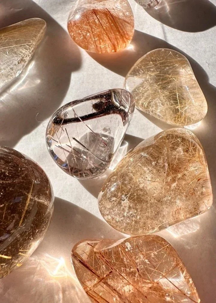 Polierte Trommelsteine mit goldenen Rutil-Einschlüssen im Sonnenlicht, hochwertige Edelsteine für Achtsamkeit und Sammlung.