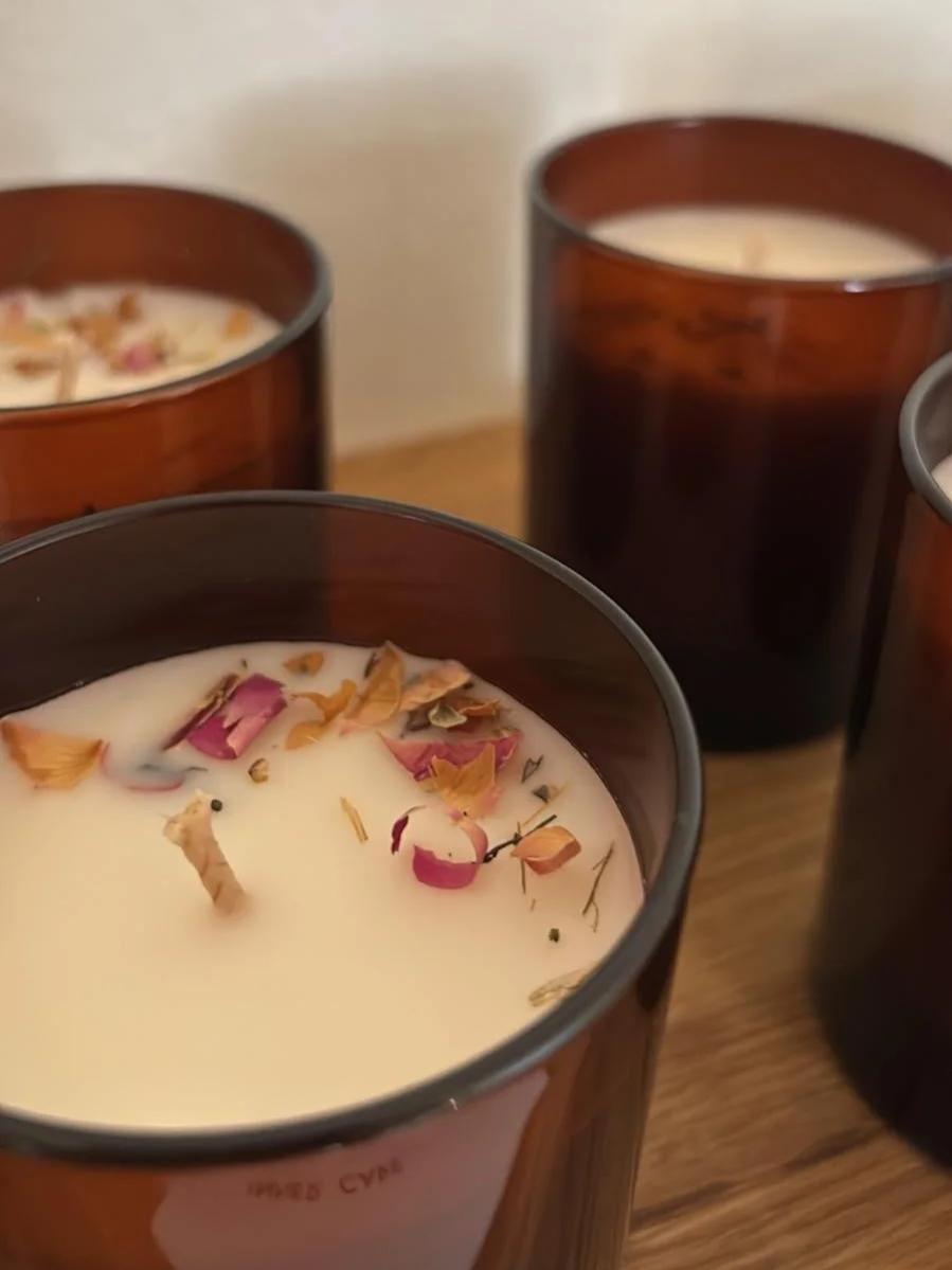 Wunderschöne Kerzen in braunem Glas, verziert mit Kräutern und Blüten, mit Intention und Magie aufgeladen