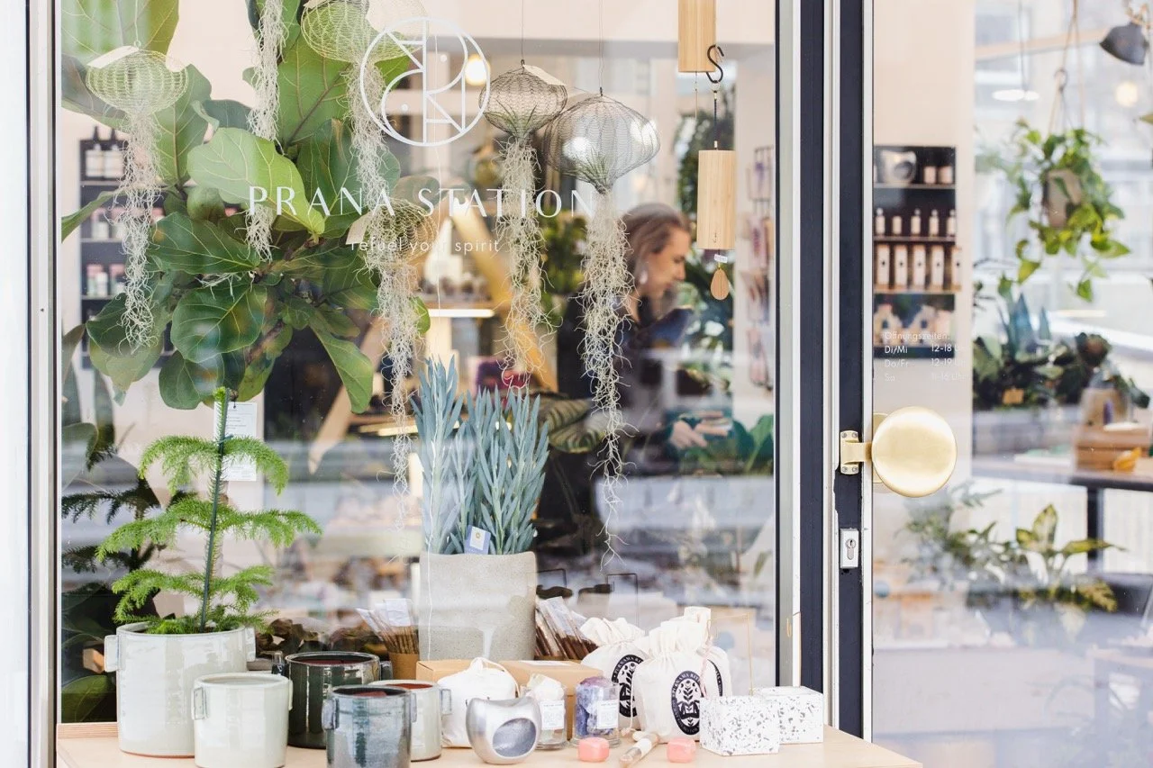Schaufenster des Prana Station Stores in Hamburg mit Pflanzen, Kerzen und Kristallen, Blick von außen in den liebevoll gestalteten Innenraum.