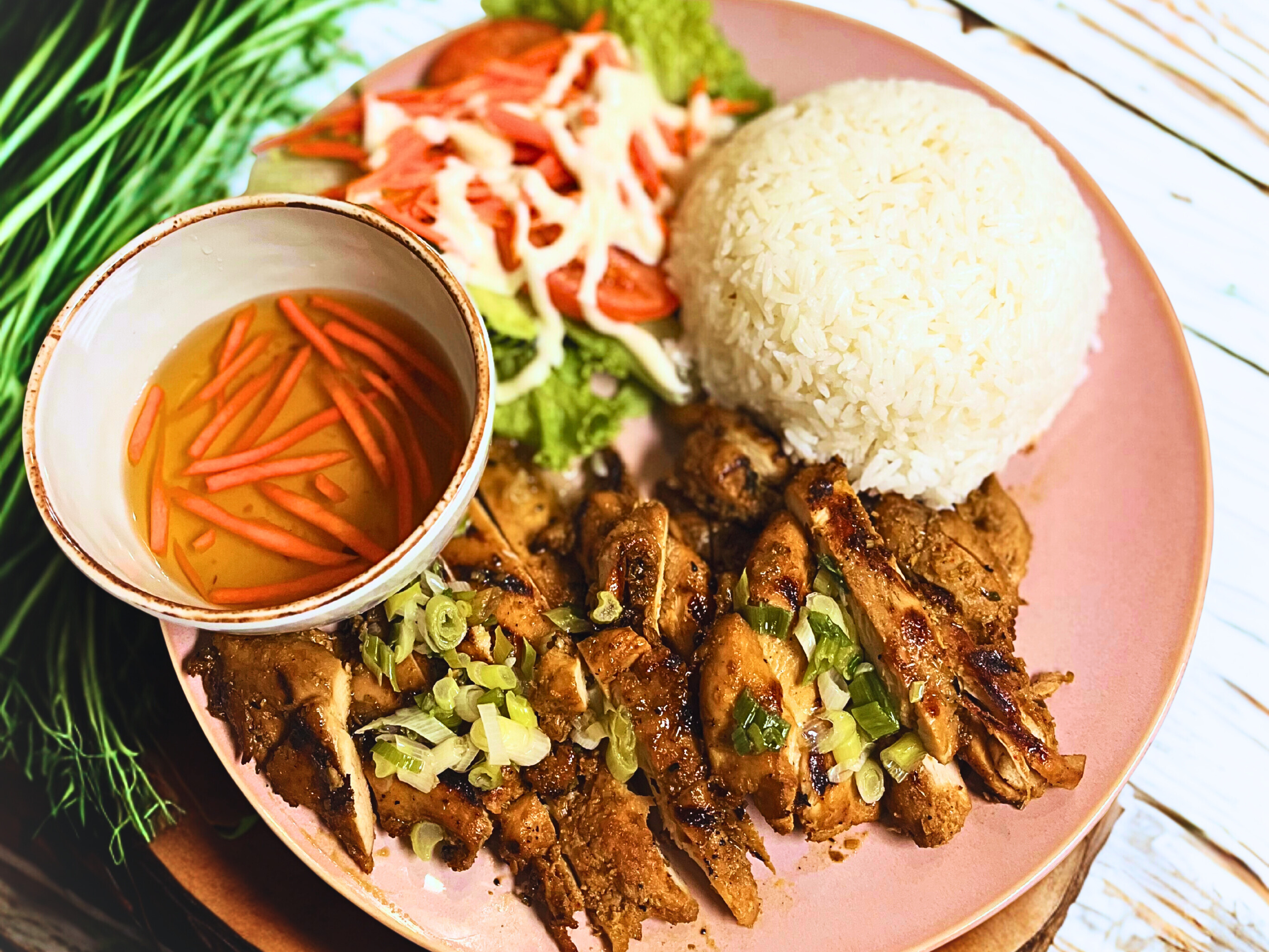 Plate with grilled meat garnished with chopped green onions, a mound of white rice, a side salad with shredded vegetables, and a small bowl of dressing with shredded carrots.