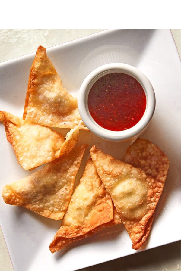 Four fried wontons with a small cup of sweet and sour sauce on a white plate.
