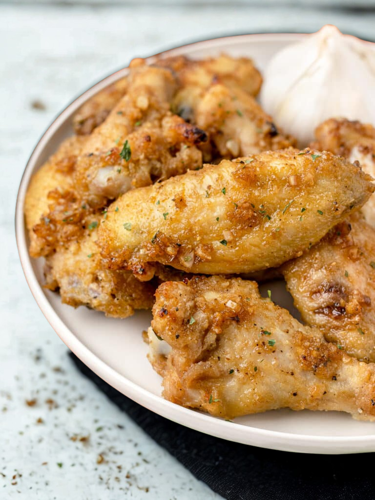 Close-up of crispy baked chicken wings sprinkled with herbs on a white plate