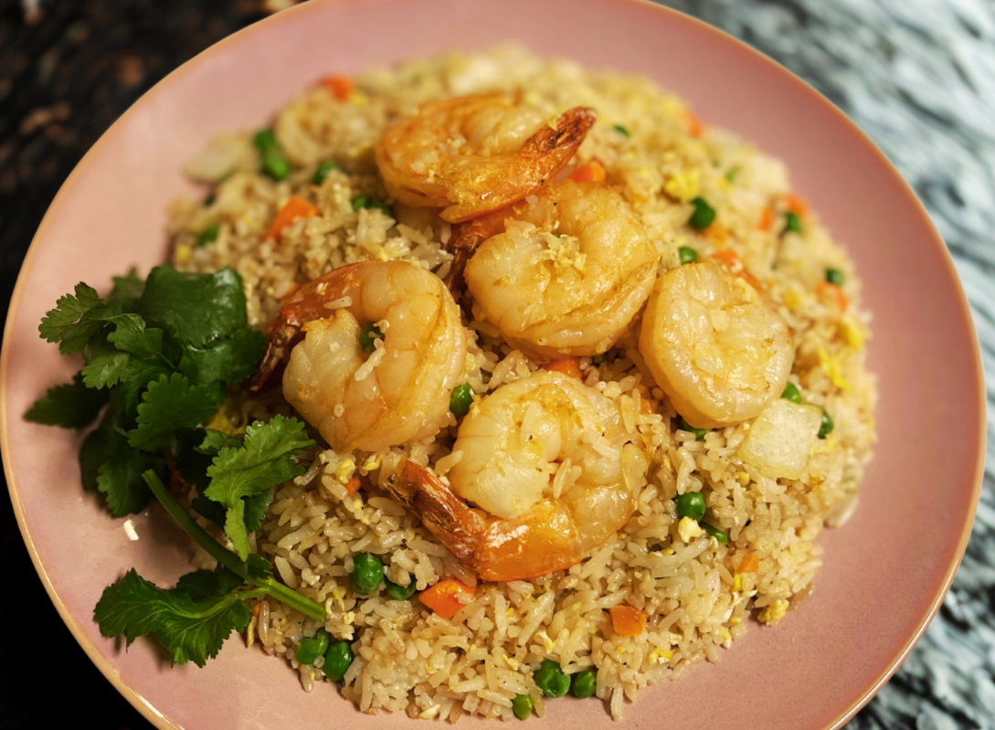 Plate of shrimp fried rice garnished with cilantro, featuring cooked shrimp, rice, peas, carrots, and scrambled egg