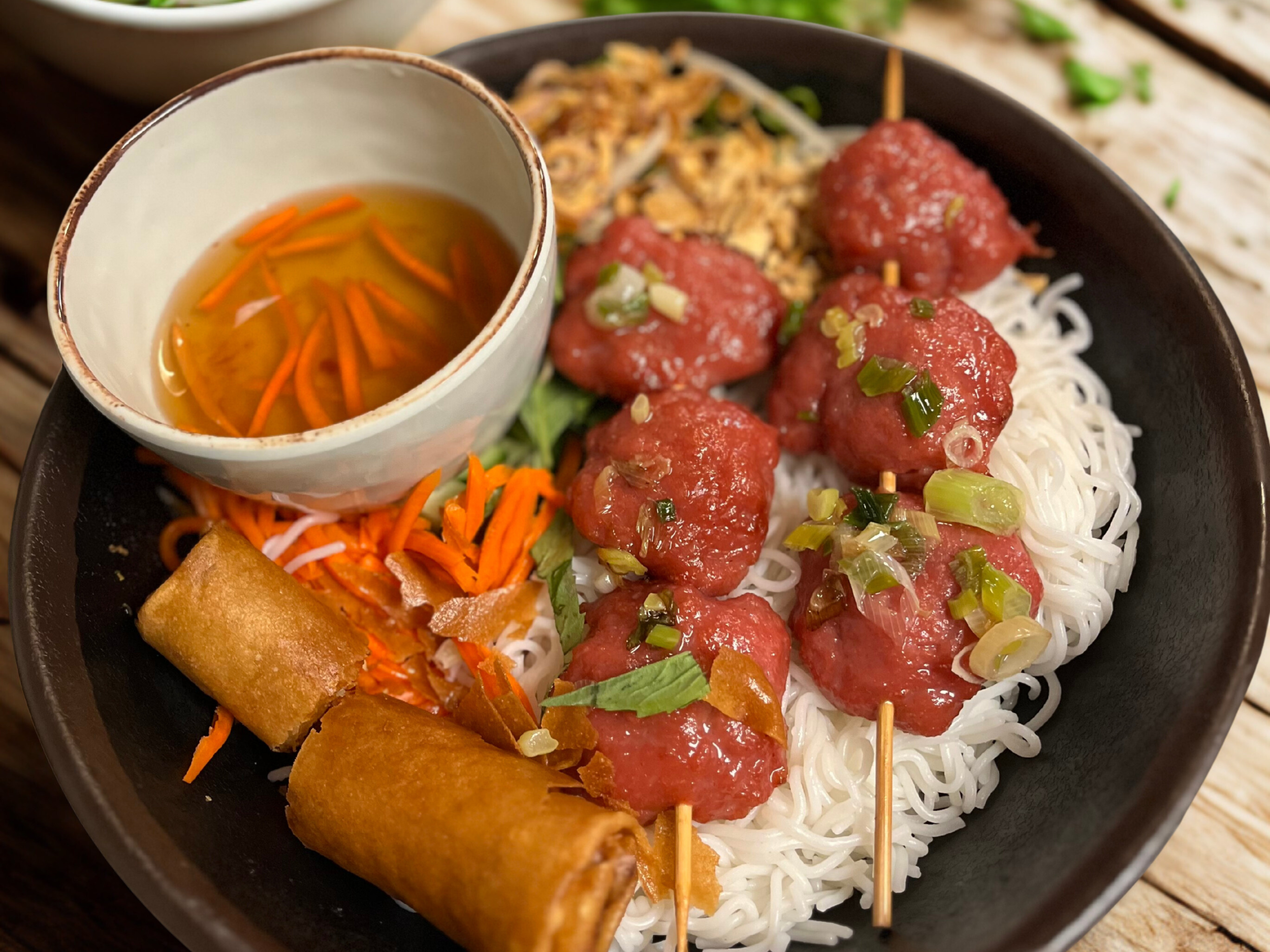 Bowl of Vietnamese bún thịt luộc with spring rolls, shredded carrots, lettuce, and dipping sauce
