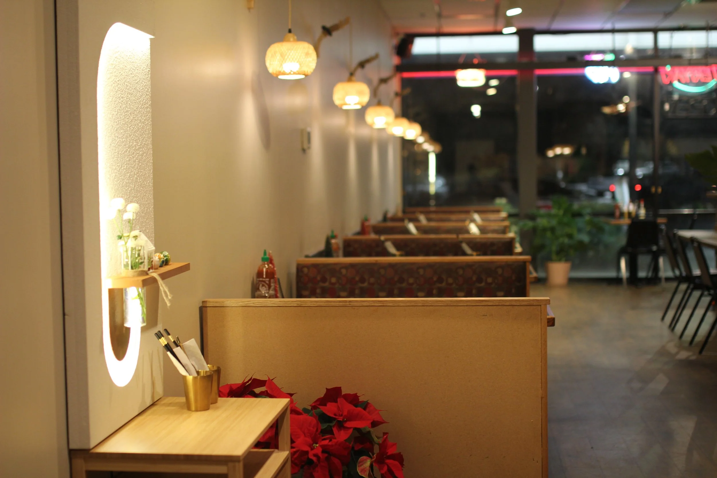 Empty restaurant booth seating area with poinsettia plants, condiment bottles, and small decor on a small table near the wall with hanging lantern-style lights.