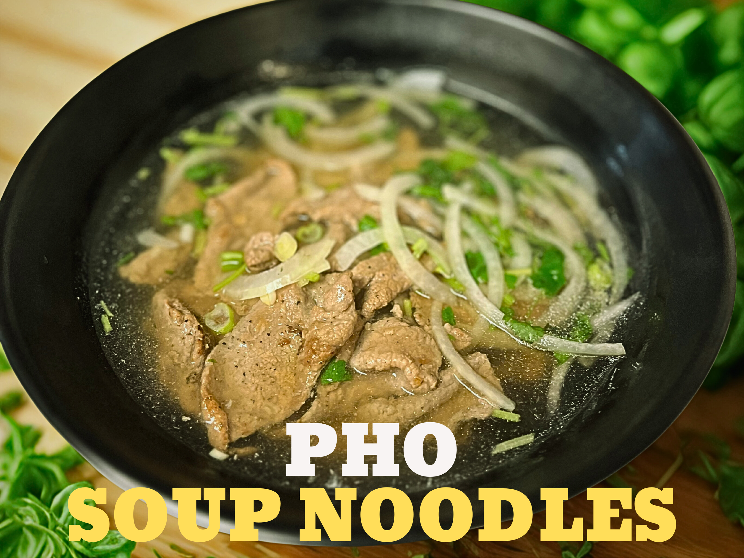 A bowl of Pho soup with sliced beef, onions, and green herbs, served in a black bowl on a wooden surface with green leafy herbs in the background.