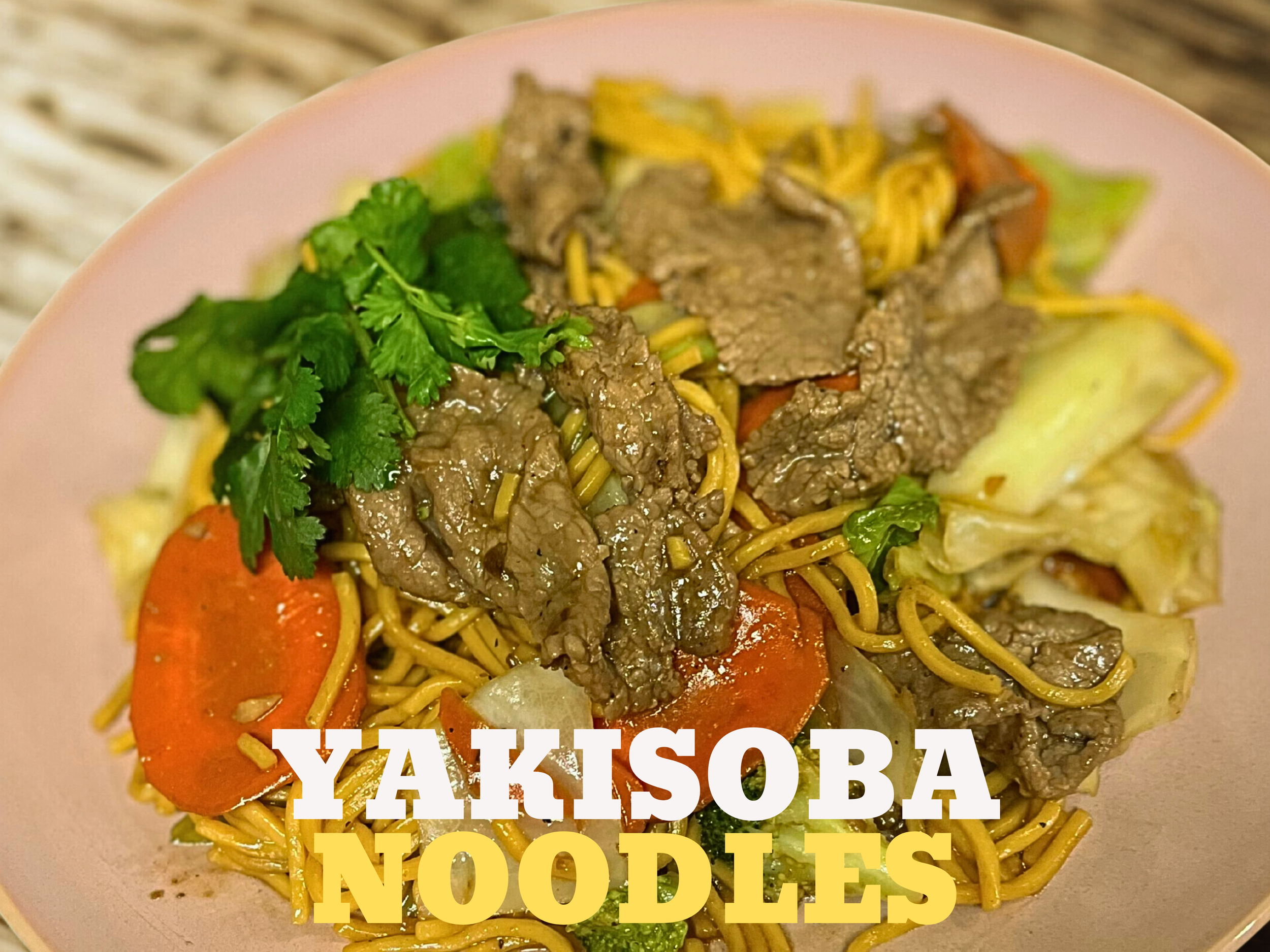 A bowl of yakisoba noodles with sliced beef, carrots, cabbage, and green herbs on a pink plate.