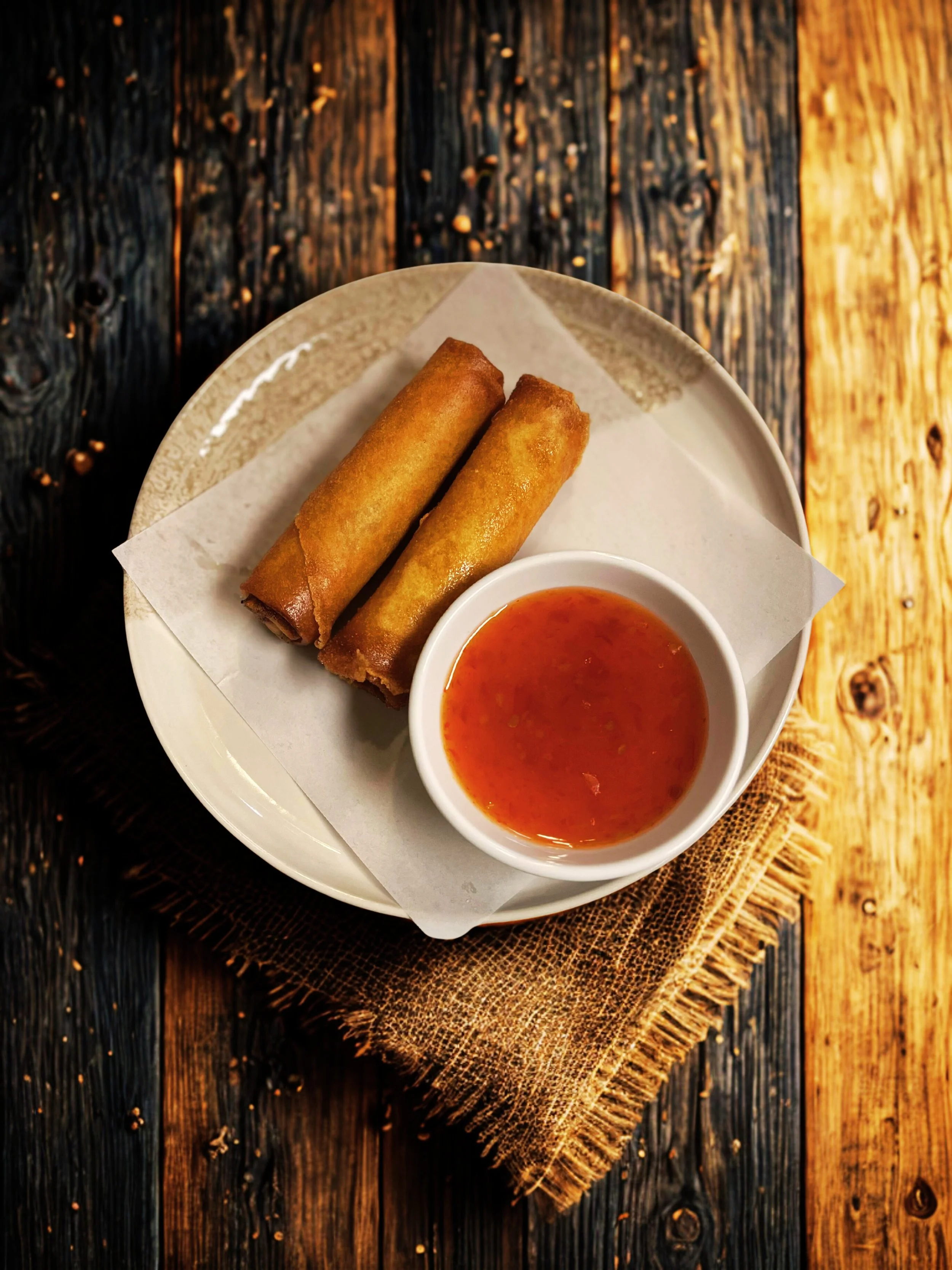 Two egg rolls with sweet and sour sauce on a white plate on a rustic wooden table.