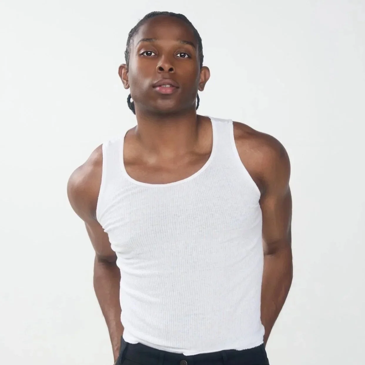 Jeune homme portant un débardeur blanc, pose contre un fond blanc.