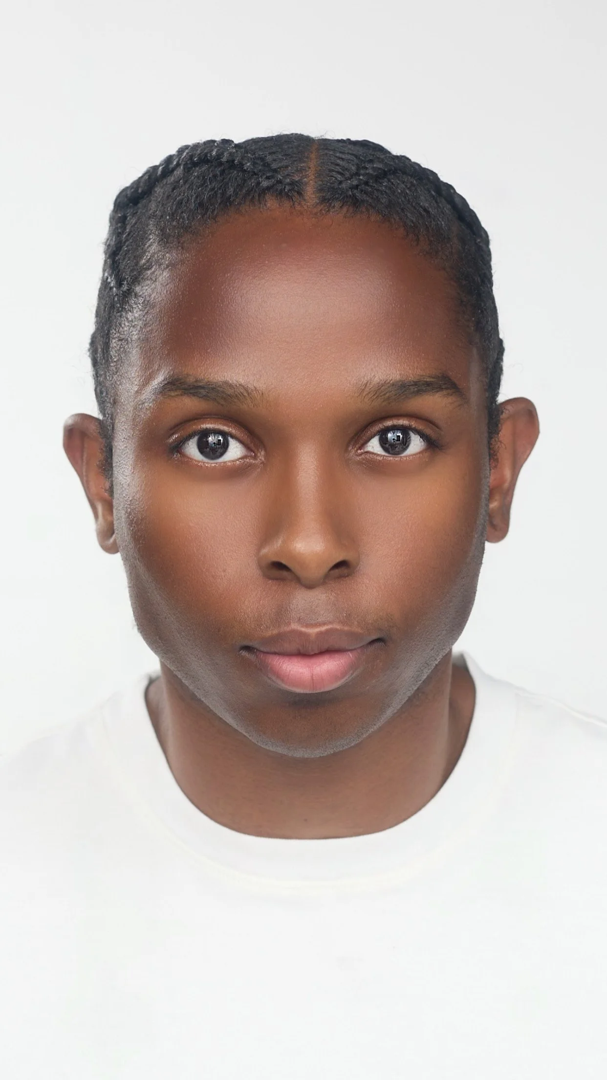 Portrait d'un homme afro-américain avec des cheveux tressés, portant un t-shirt blanc, fond blanc.