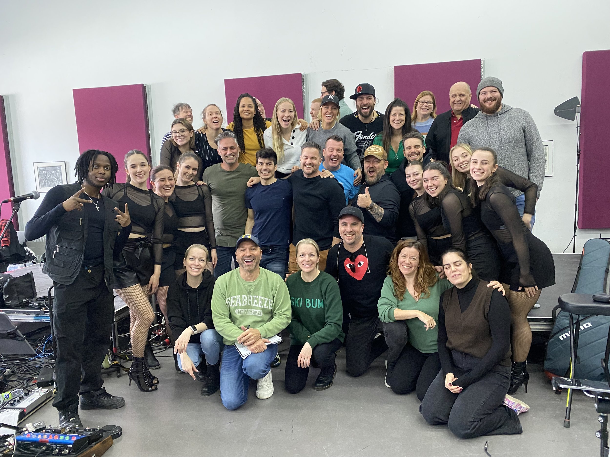 Groupe de personnes posant ensemble, souriant, dans une pièce avec des panneaux acoustiques violets.